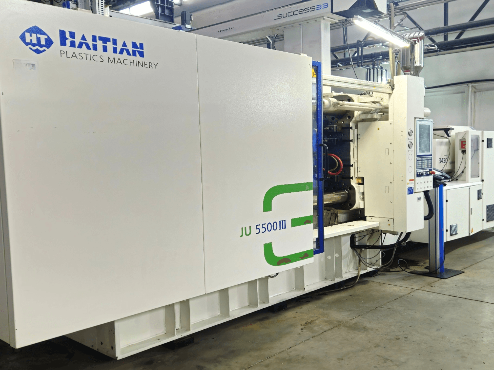 Haïtiaanse JU 5500III kunststofmachines in een fabrieksomgeving, vooraanzicht met bedieningspaneel en productiegebied.