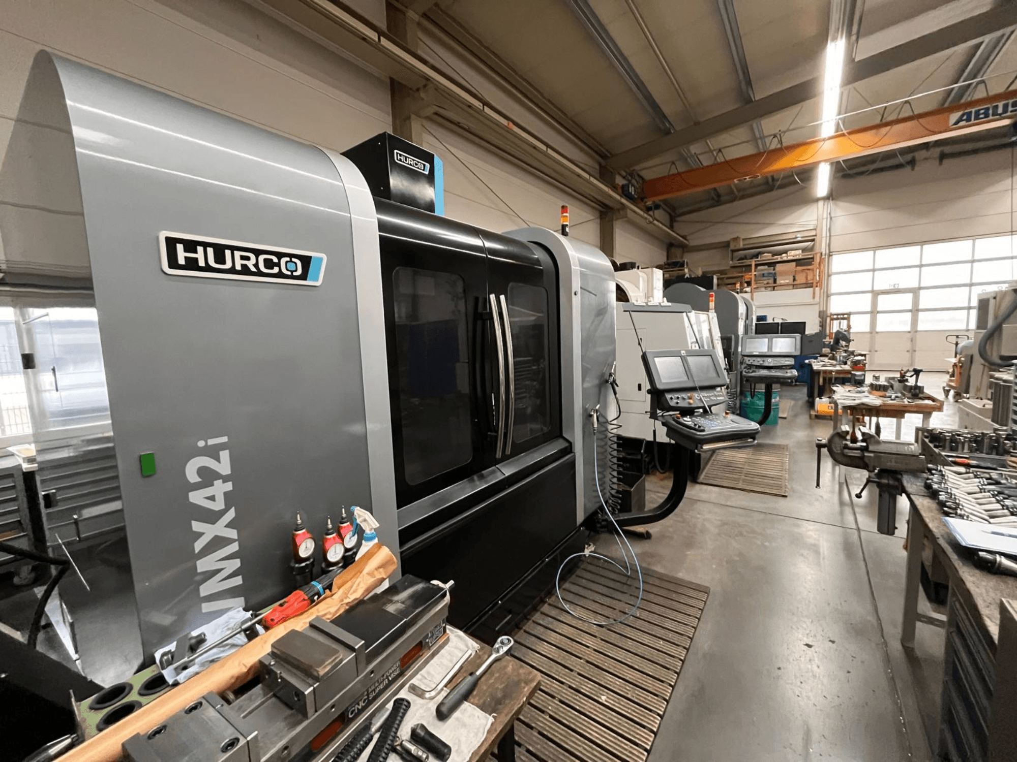 Hurco VMX42i CNC machine in een werkplaats, vooraanzicht. Kenmerken bedieningspaneel, grijze behuizing en industriële omgeving.