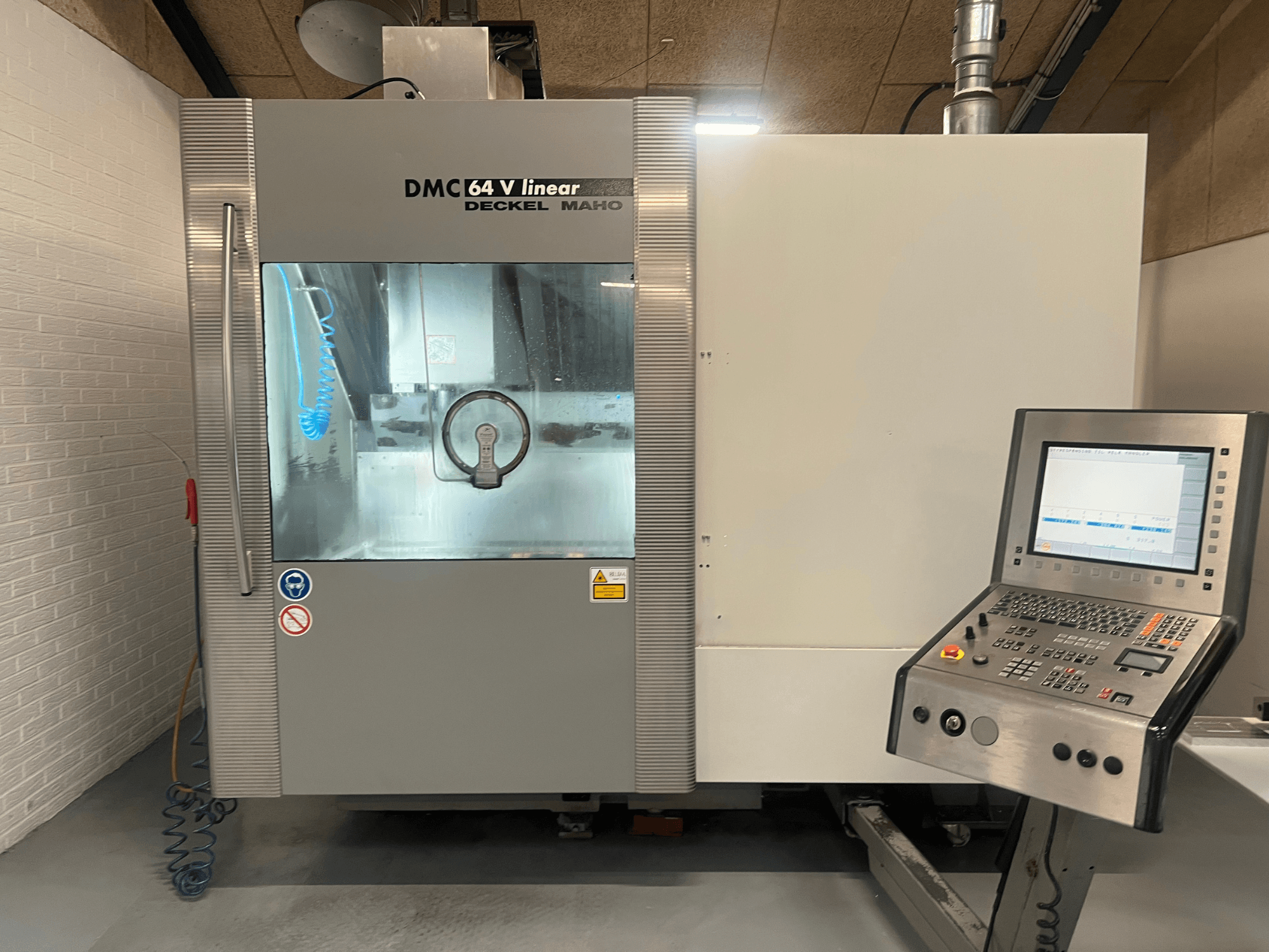 DMC 64 V Linear van Deckel Maho, vooraanzicht van CNC-bewerkingscentrum met bedieningspaneel en koelpijp zichtbaar.