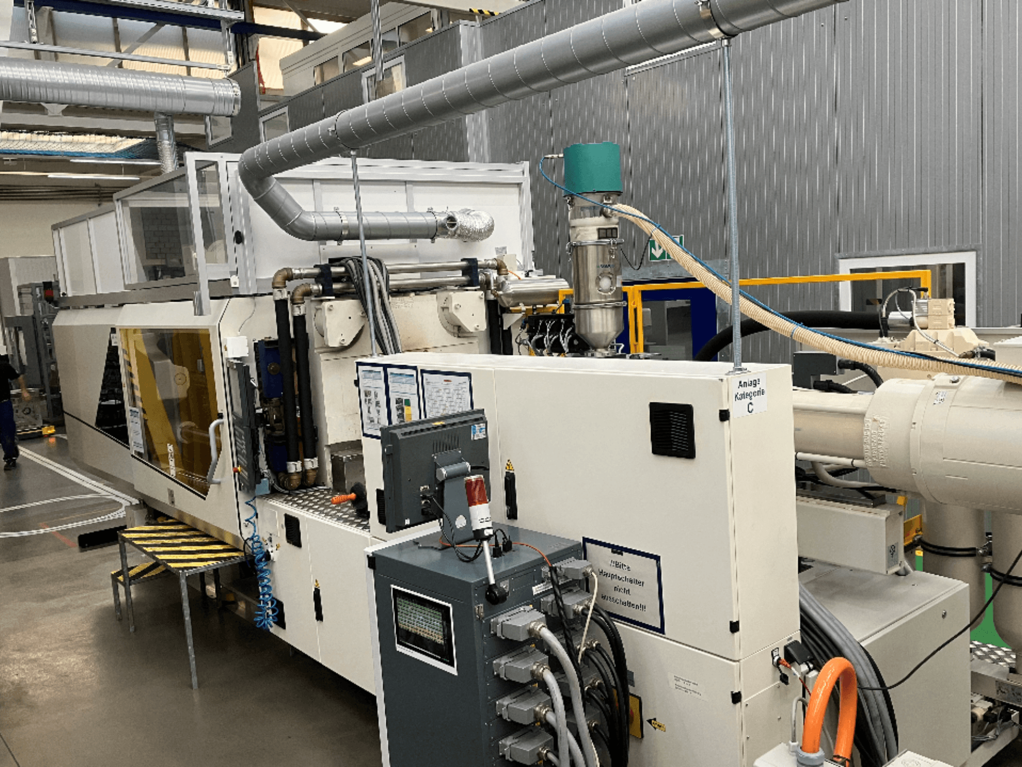 Spuitgietmachine, vooraanzicht, met merklabel, bedieningspaneel en zichtbare slangen in een fabrieksomgeving.