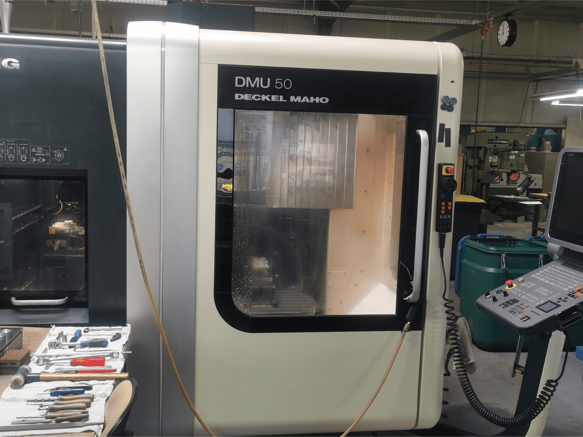 DMU 50 deckel maho CNC machine gezien vanaf de voorkant, met het bedieningspaneel en de transparante deur. Gereedschap is vlakbij.