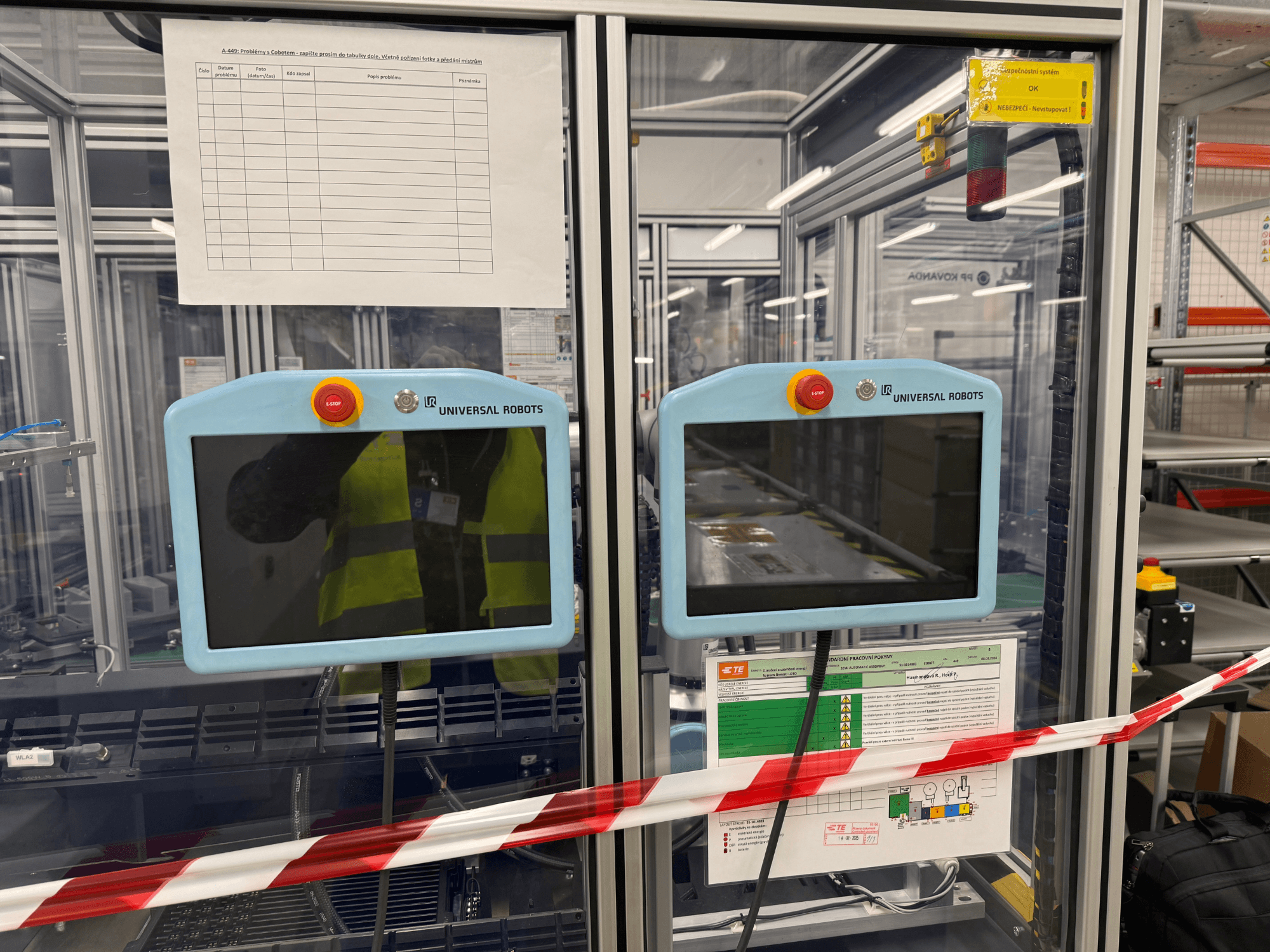 Bedieningspaneel voor de Universal Robots UR5 e robotarm, met twee monitoren, noodstopknoppen en veiligheidsinstructies.