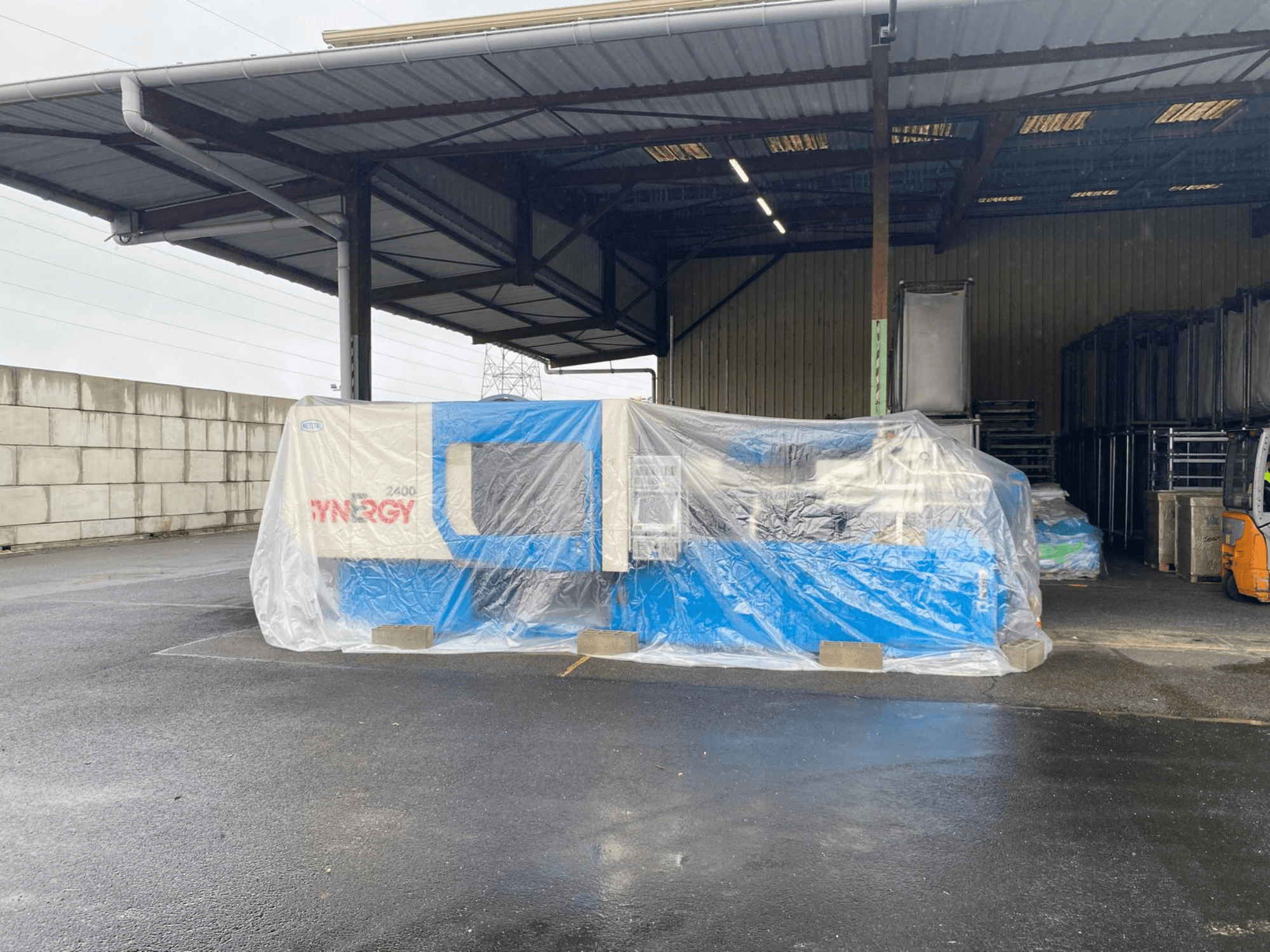 Ingewikkelde SYNERGY 2400 machine gezien vanaf de voorkant, blauwe en beige kleuren, in een grote overdekte industriële ruimte.