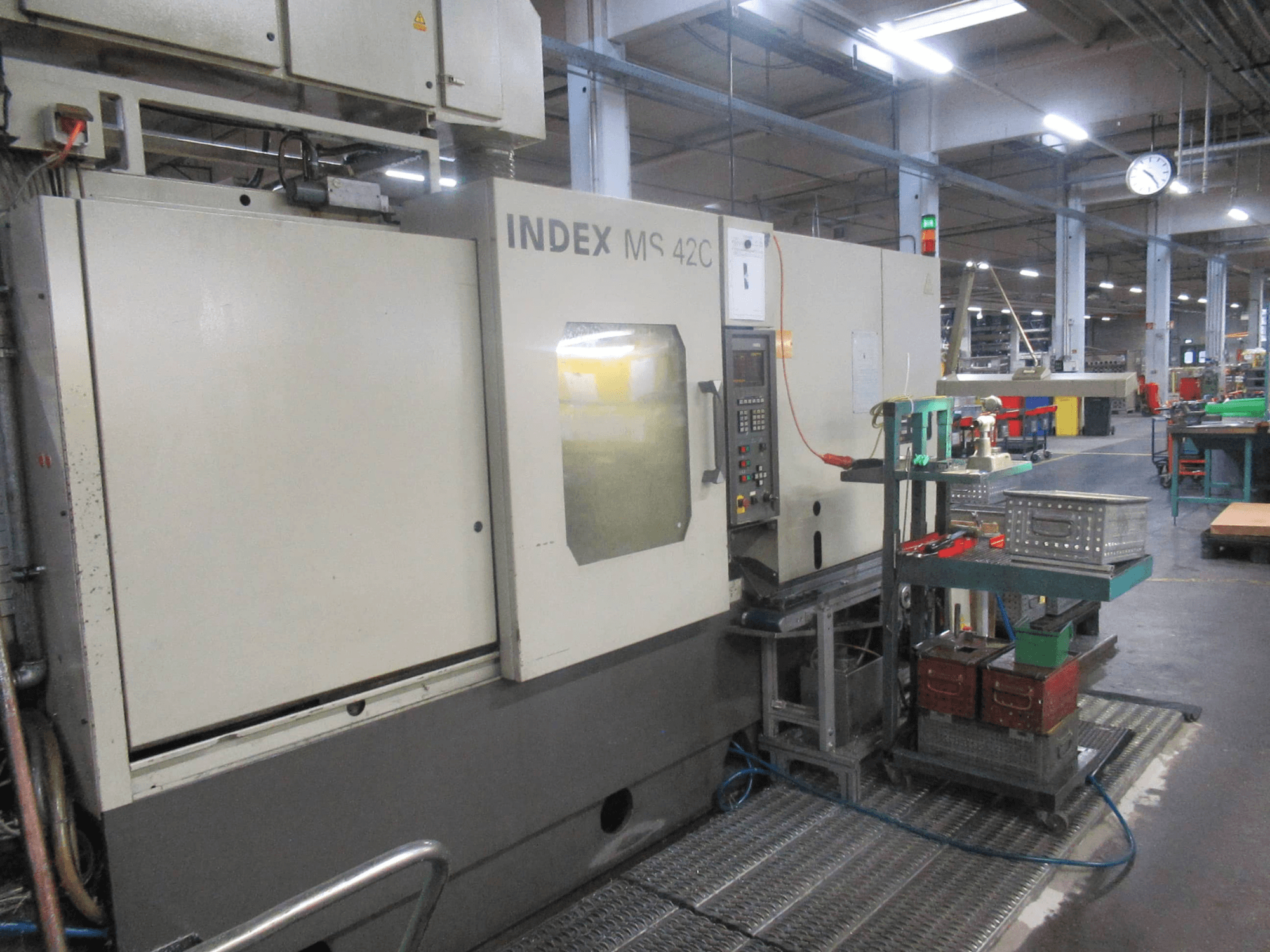 INDEX MS 42C CNC machine in een werkplaats, zijaanzicht met bedieningspaneel en gereedschapopslag op verrijdbaar onderstel.