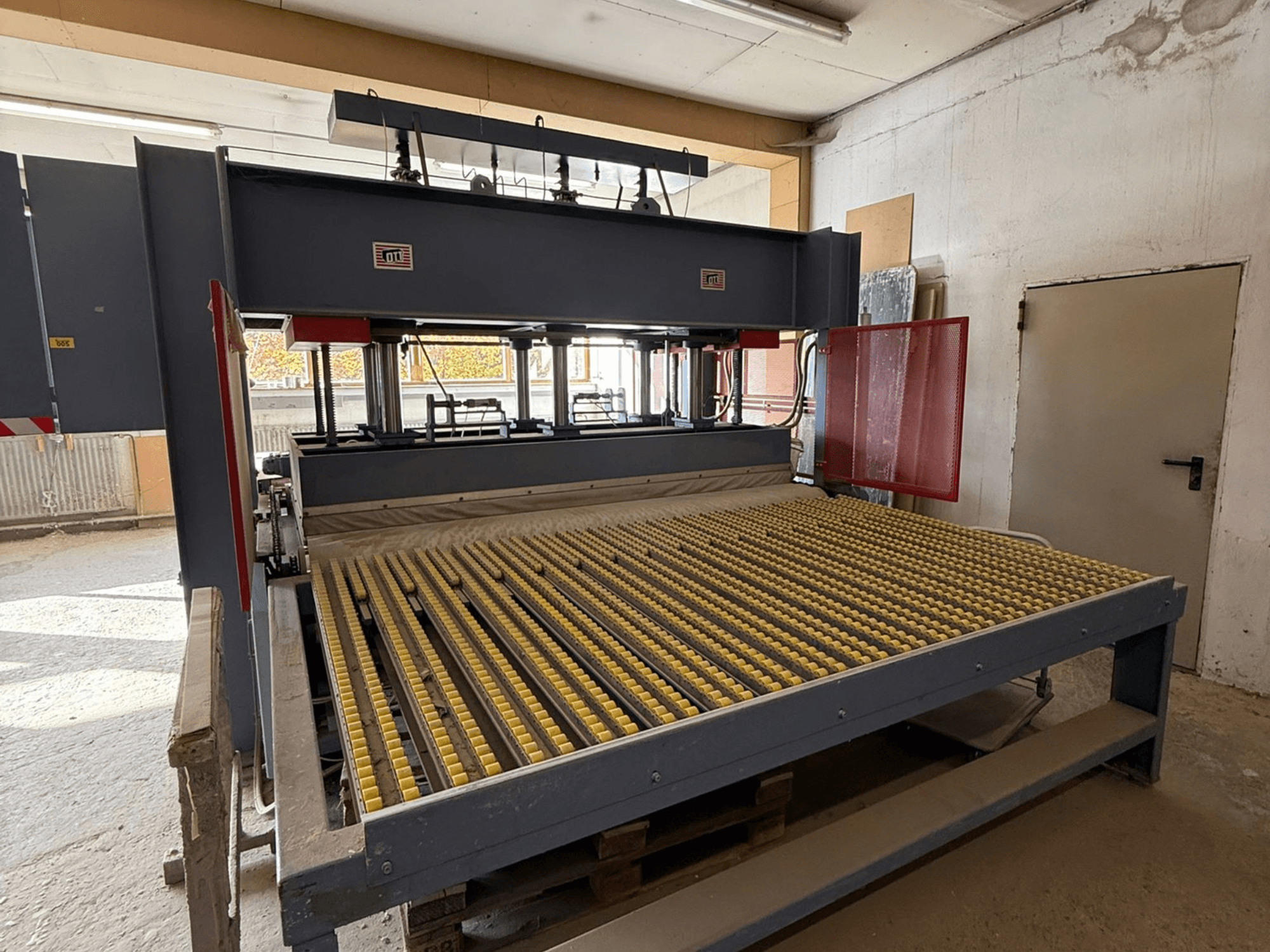 Industriële machine met gele rollen, vooraanzicht, merklogo zichtbaar, gebruikt voor het verwerken van materialen in een werkplaats.