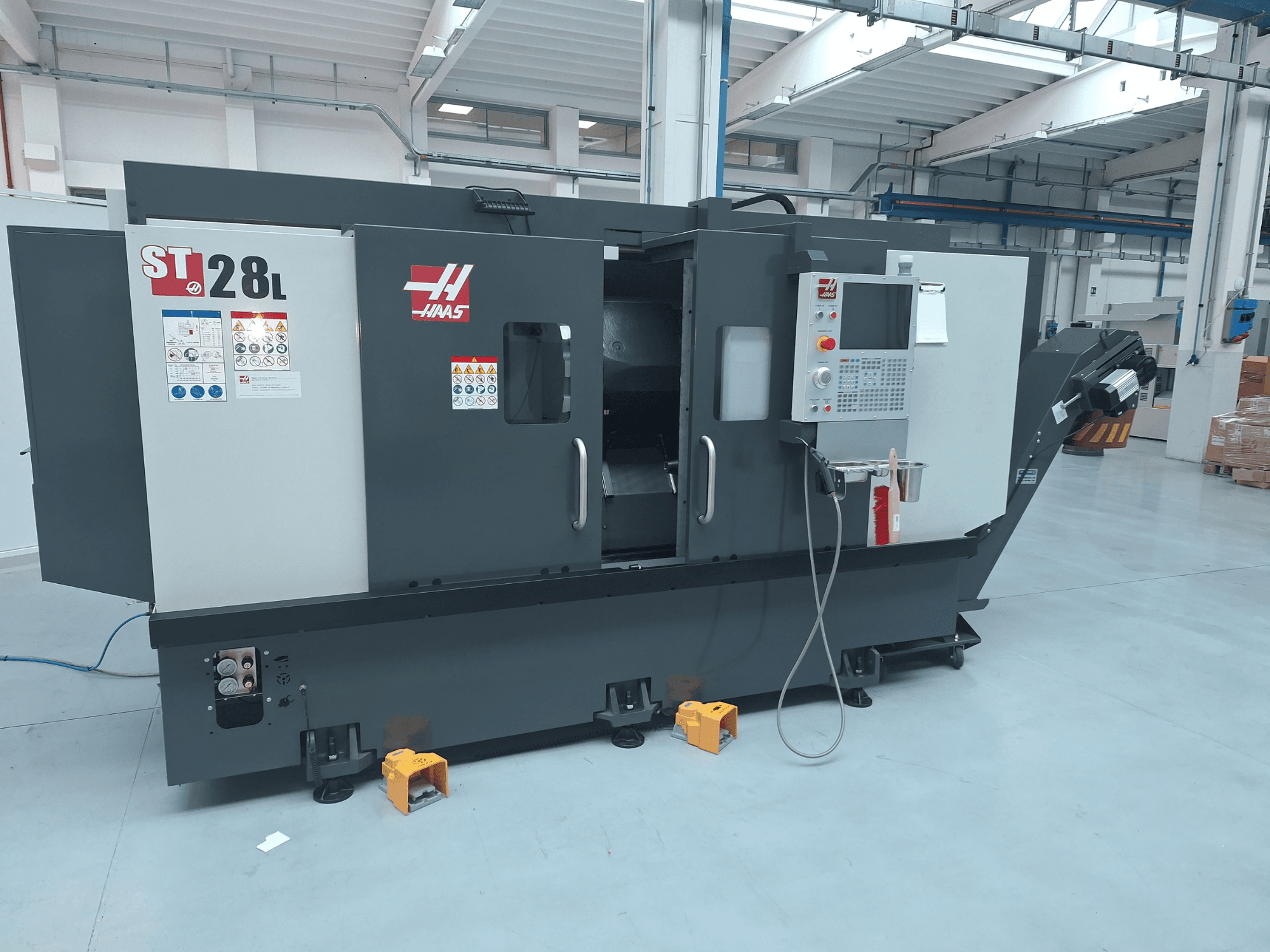 Zijaanzicht van de Haas ST-28L horizontale draaimachine, met bedieningspaneel, bedieningsknoppen en veiligheidslabels.