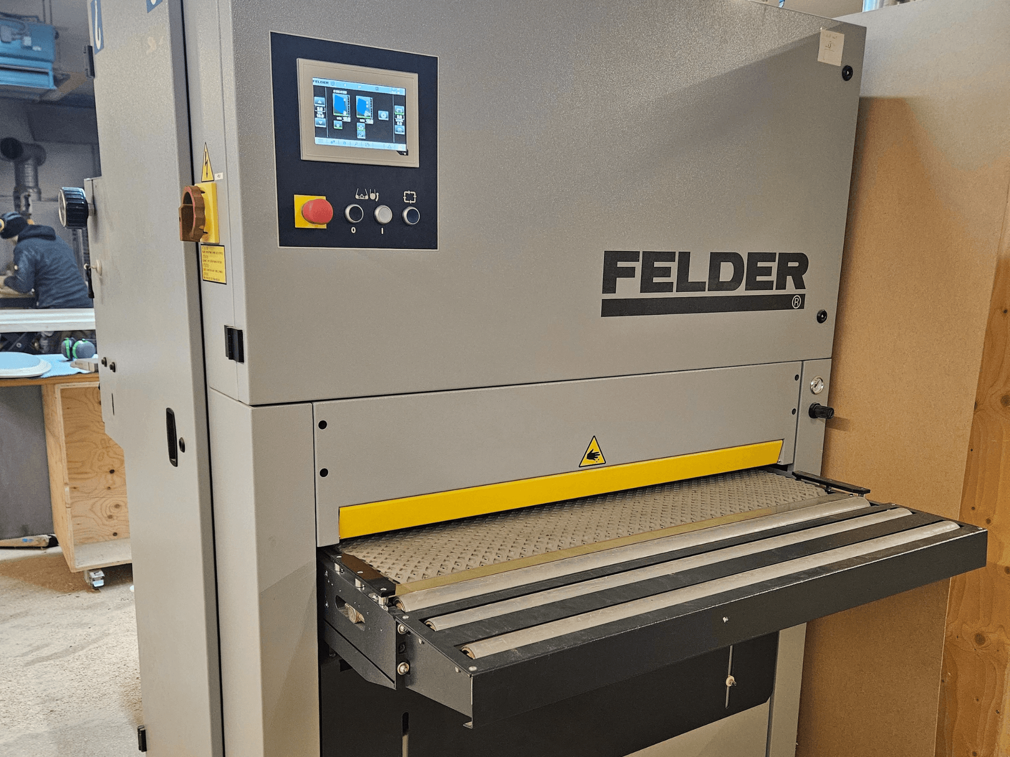 FELDER houtbewerkingsmachine in vooraanzicht, met digitaal bedieningspaneel en gele invoertafel met veiligheidswaarschuwingen.