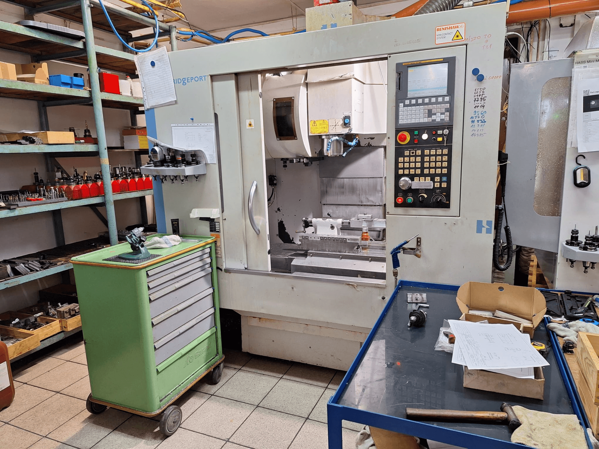 Vooraanzicht van het verticale bewerkingscentrum Hardinge Bridgeport GX 710 met bedieningspaneel, gereedschappen en planken in een werkplaatsomgeving.