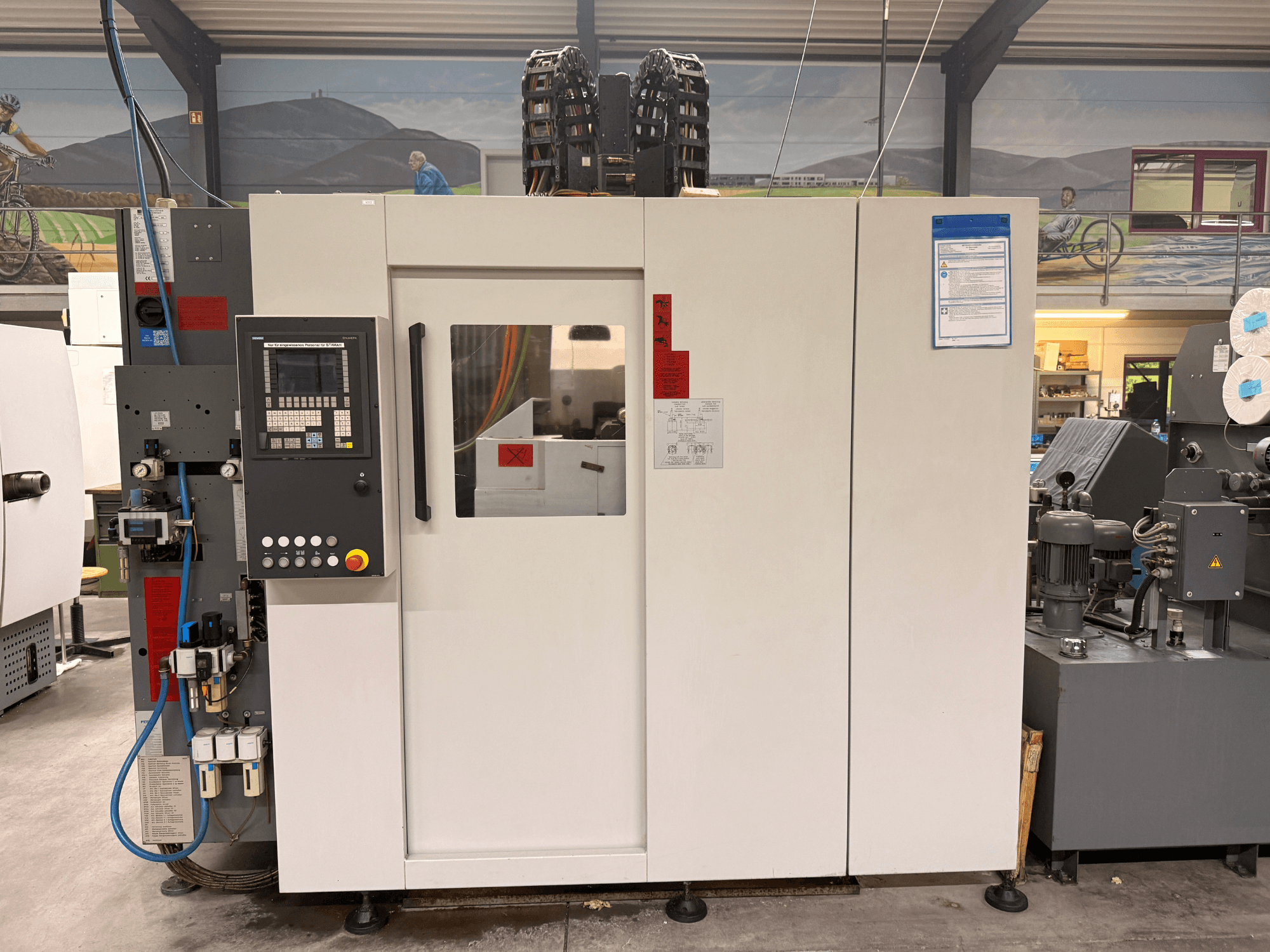 Wit CNC-bewerkingscentrum met bedieningspaneel, vooraanzicht, met knoppen en digitaal display, in een werkplaats.