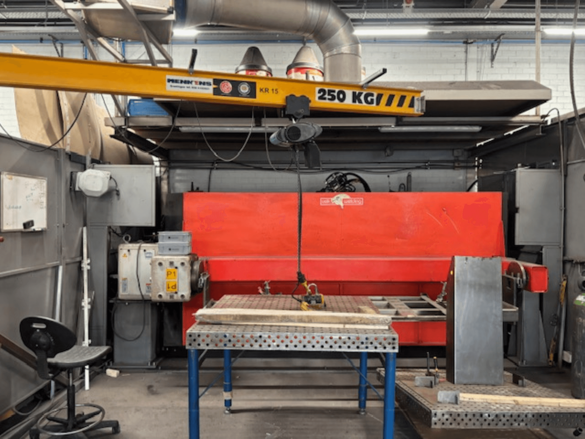 Industriële werkplaats met een rode hydraulische pers, een bovenloopkraan met het opschrift "KR 15" en een metalen werktafel, zijaanzicht perspectief.
