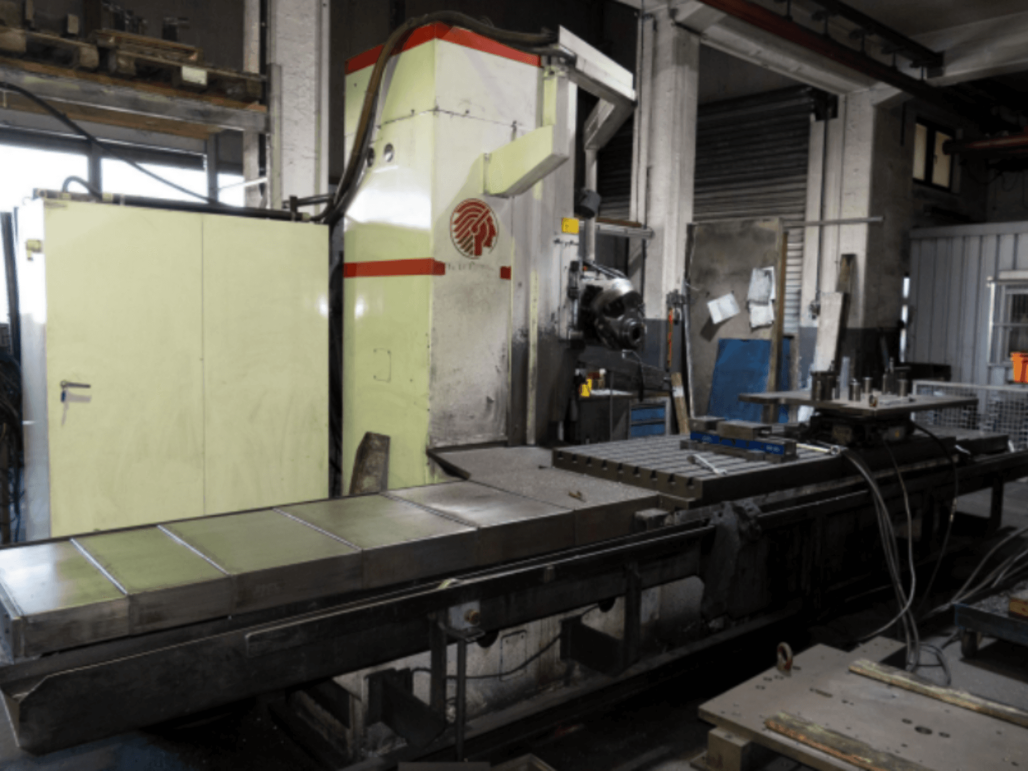 Industriële freesmachine met een grote tafel, zijaanzicht, waarop de bedieningselementen en hulpstukken in een werkplaatsomgeving te zien zijn.