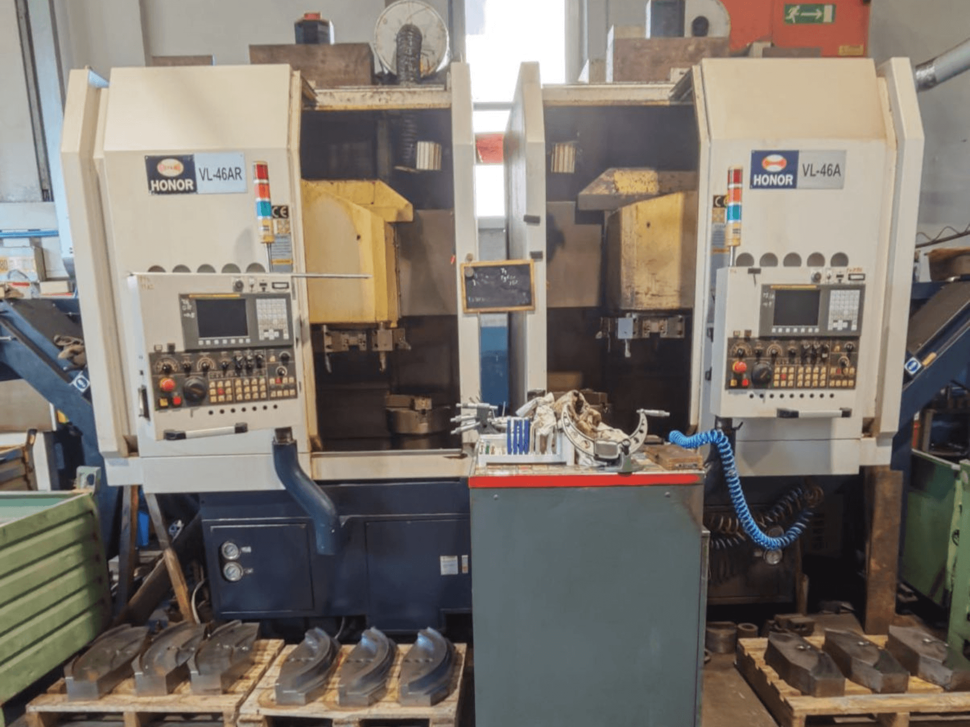 Vooraanzicht van de HONOR SEIKI VL 46A verticale draaibank, met het bedieningspaneel en de omliggende onderdelen op houten pallets.