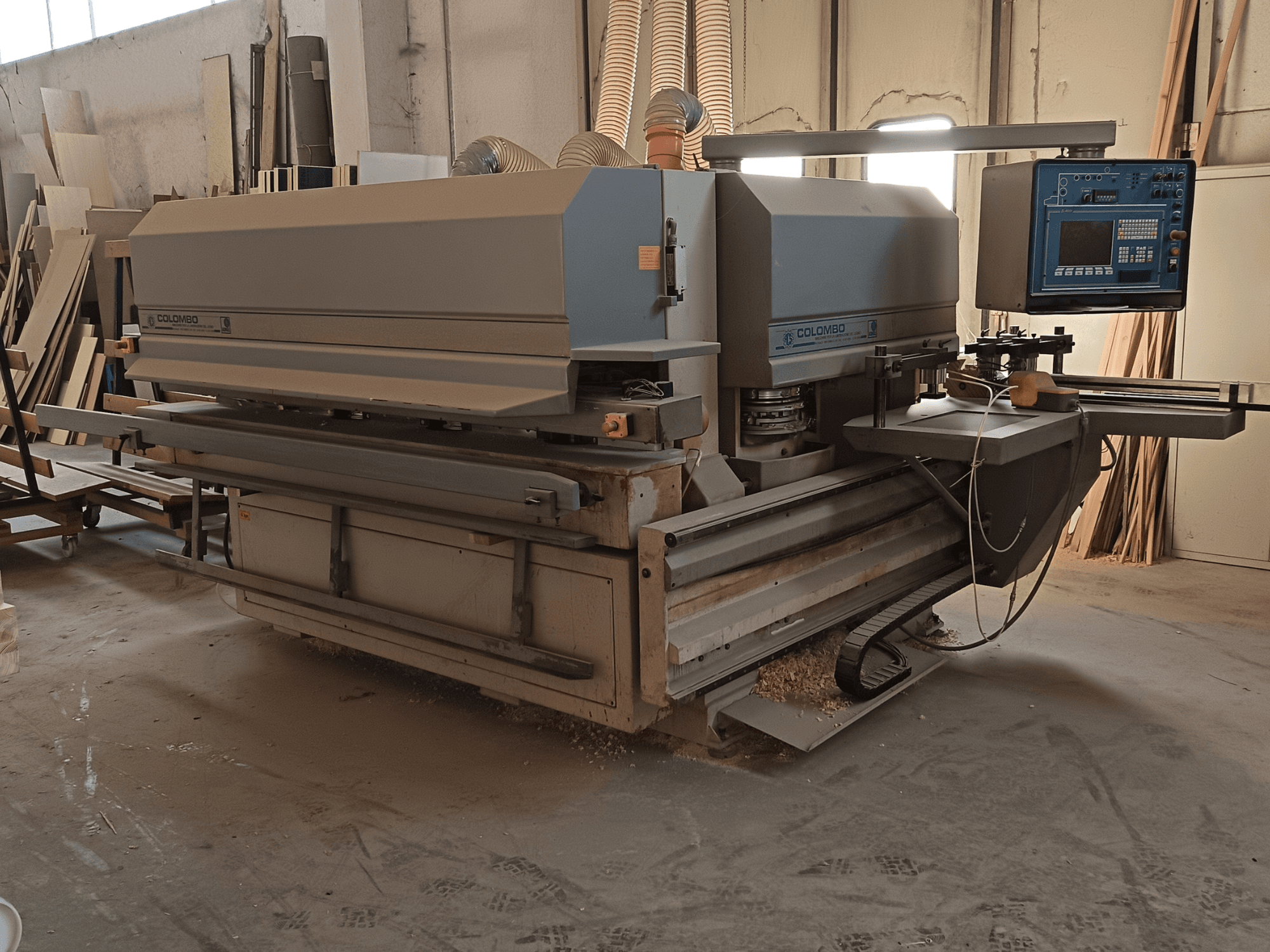 Colombo houtbewerkingsmachine, zijaanzicht, met het bedieningspaneel, zaagbladen en zaagstofophoping in de werkplaats.