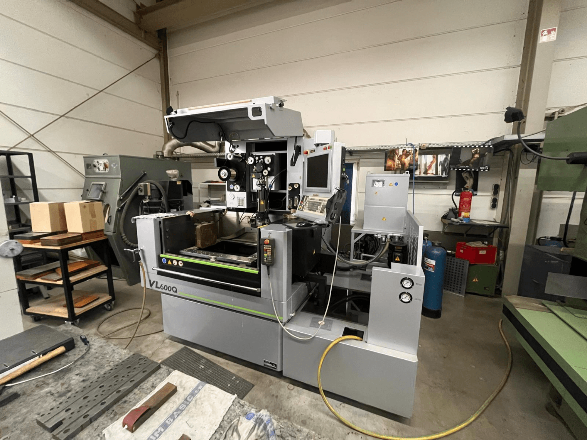 VL600Q CNC machine in een werkplaats, vooraanzicht, met bedieningspaneel, geplaatst materiaal en diverse gereedschappen in de buurt.
