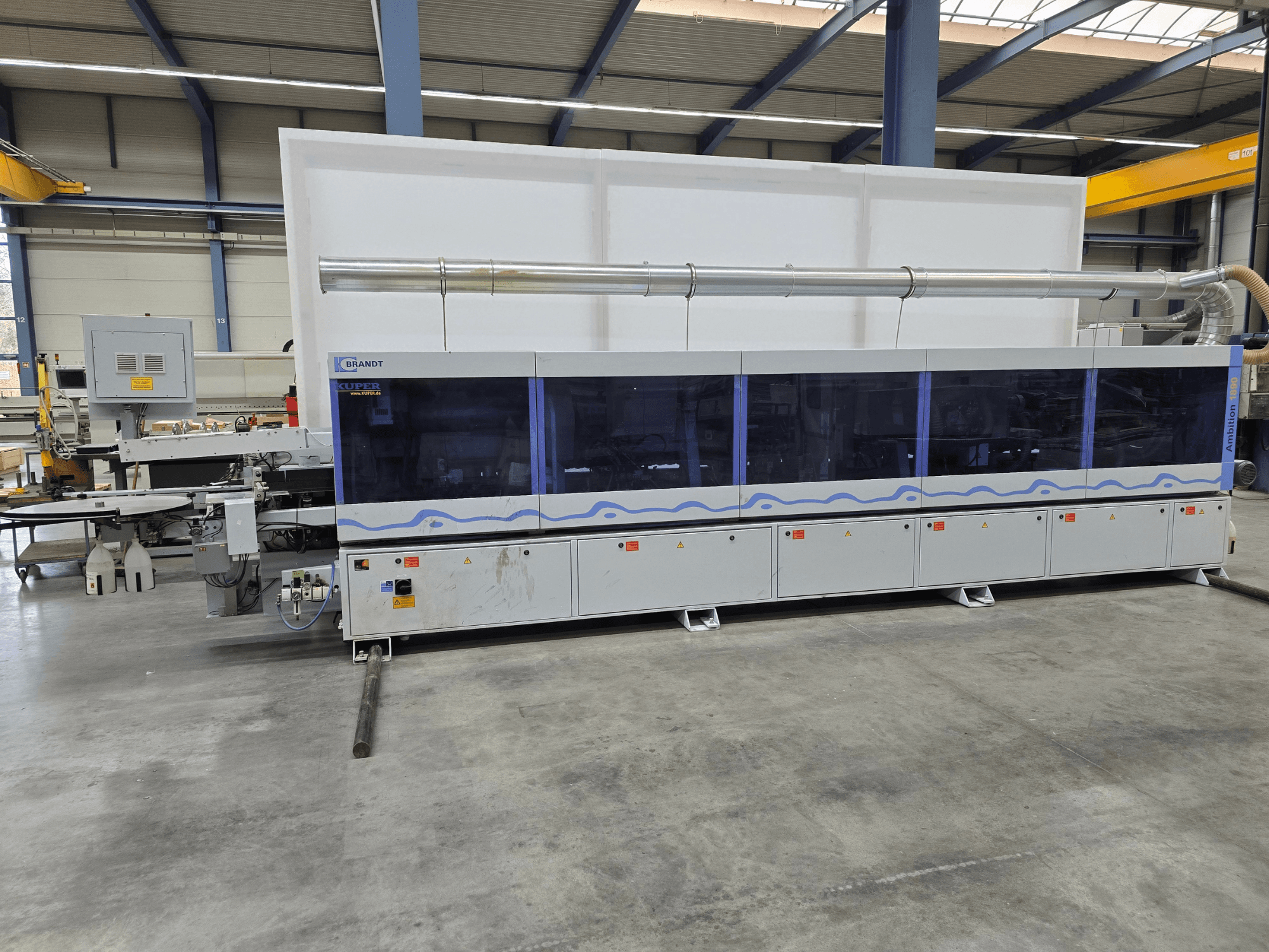 Brandt KUPER machine in een fabriek, vooraanzicht met transparante panelen, met bedieningsknoppen en veiligheidswaarschuwingen.