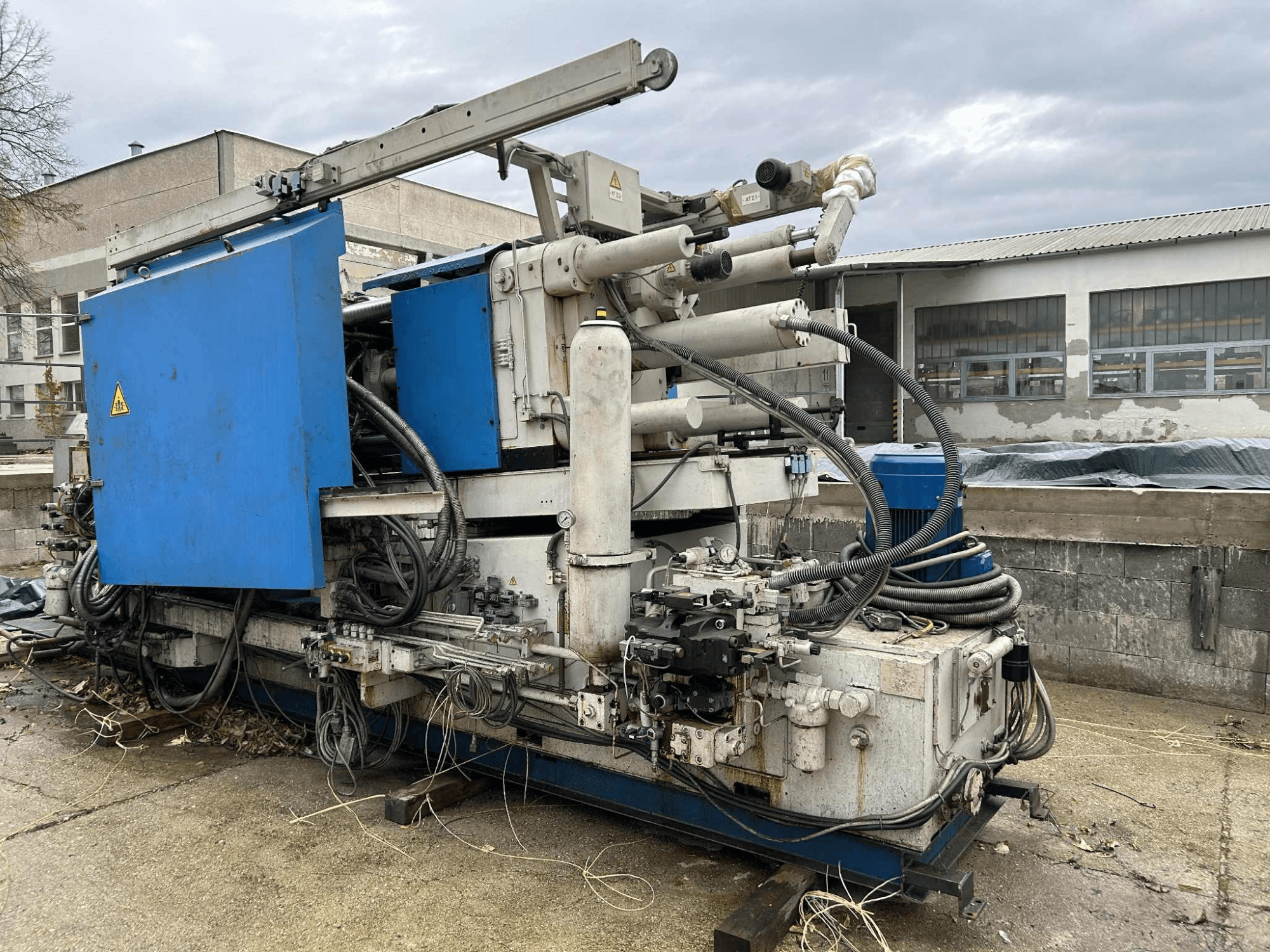 Grote industriële hydraulische machine met blauwe behuizing, verschillende slangen en metalen onderdelen, gezien vanaf de zijkant.