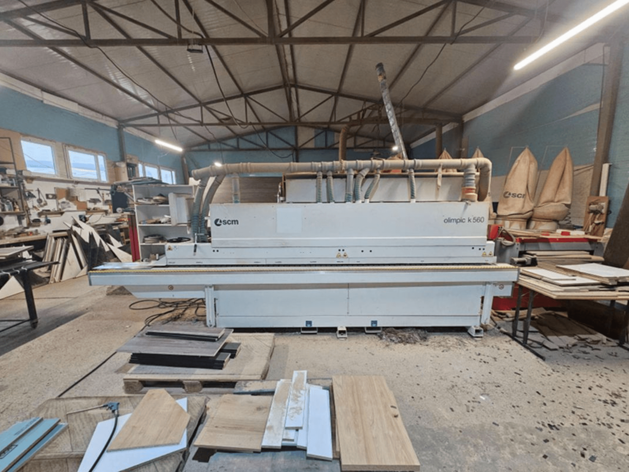 De SCM Olimpic K 560 kantenlijmmachine, afgebeeld in een werkplaats, vooraanzicht; zichtbare onderdelen zijn onder meer de invoerrollen en het afzuigsysteem.