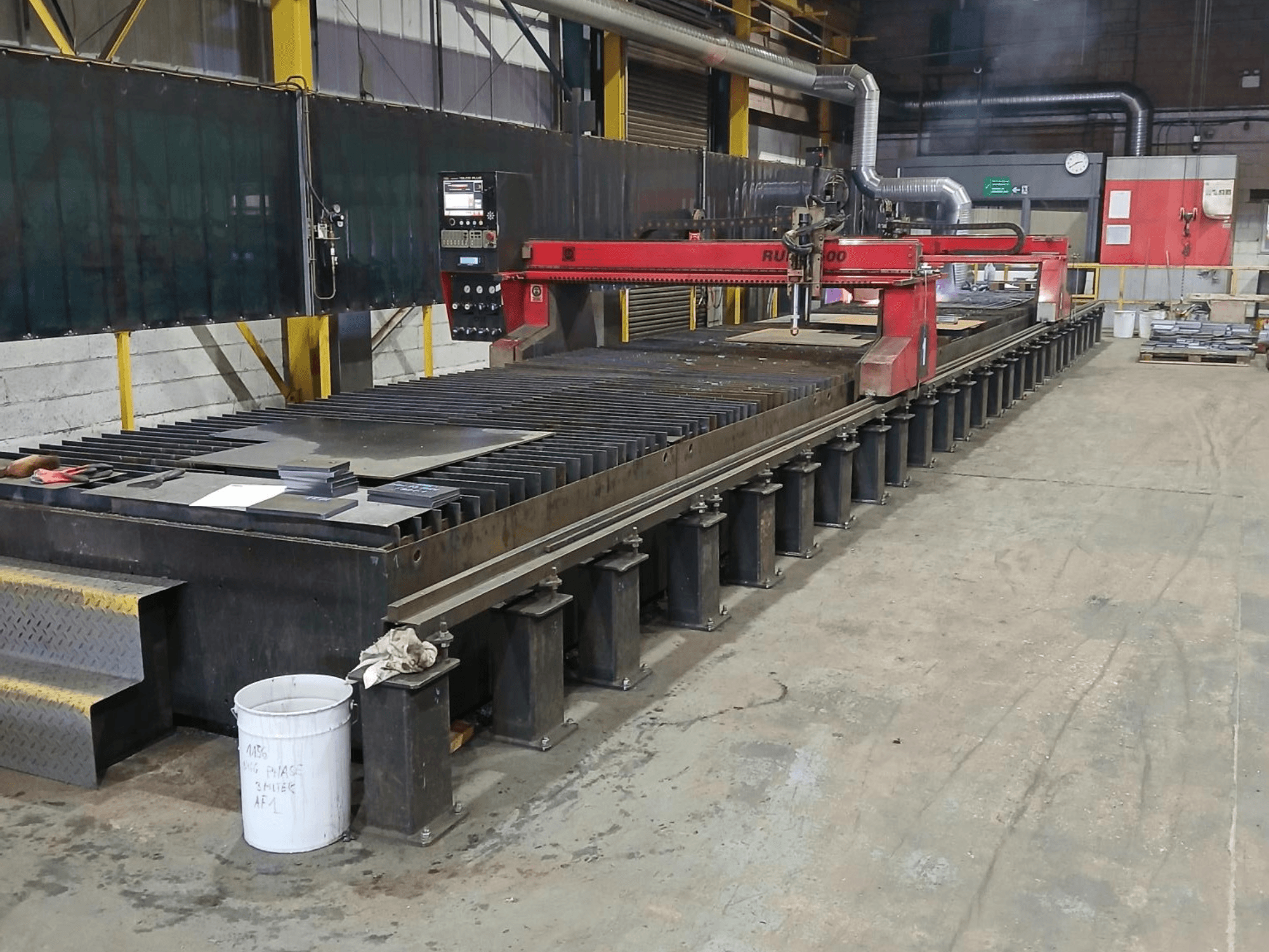 Rode RUIDA 300 snijmachine, zijaanzicht, met metalen plaat op een stalen tafel, in een industriële werkruimte.