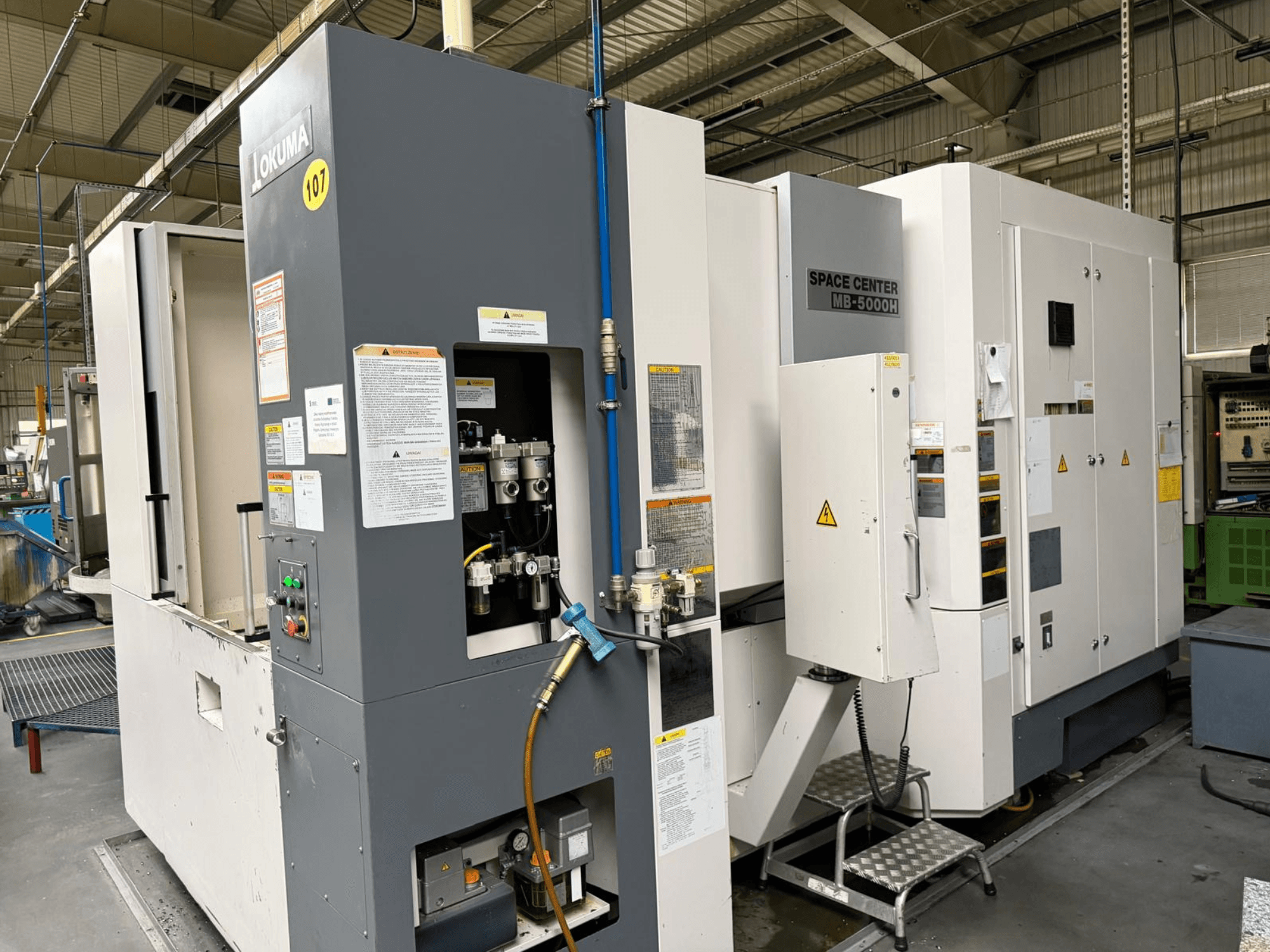 Okuma MB 5000H horizontaal bewerkingscentrum, zijaanzicht met bedieningspaneel en machineonderdelen in een fabrieksomgeving.