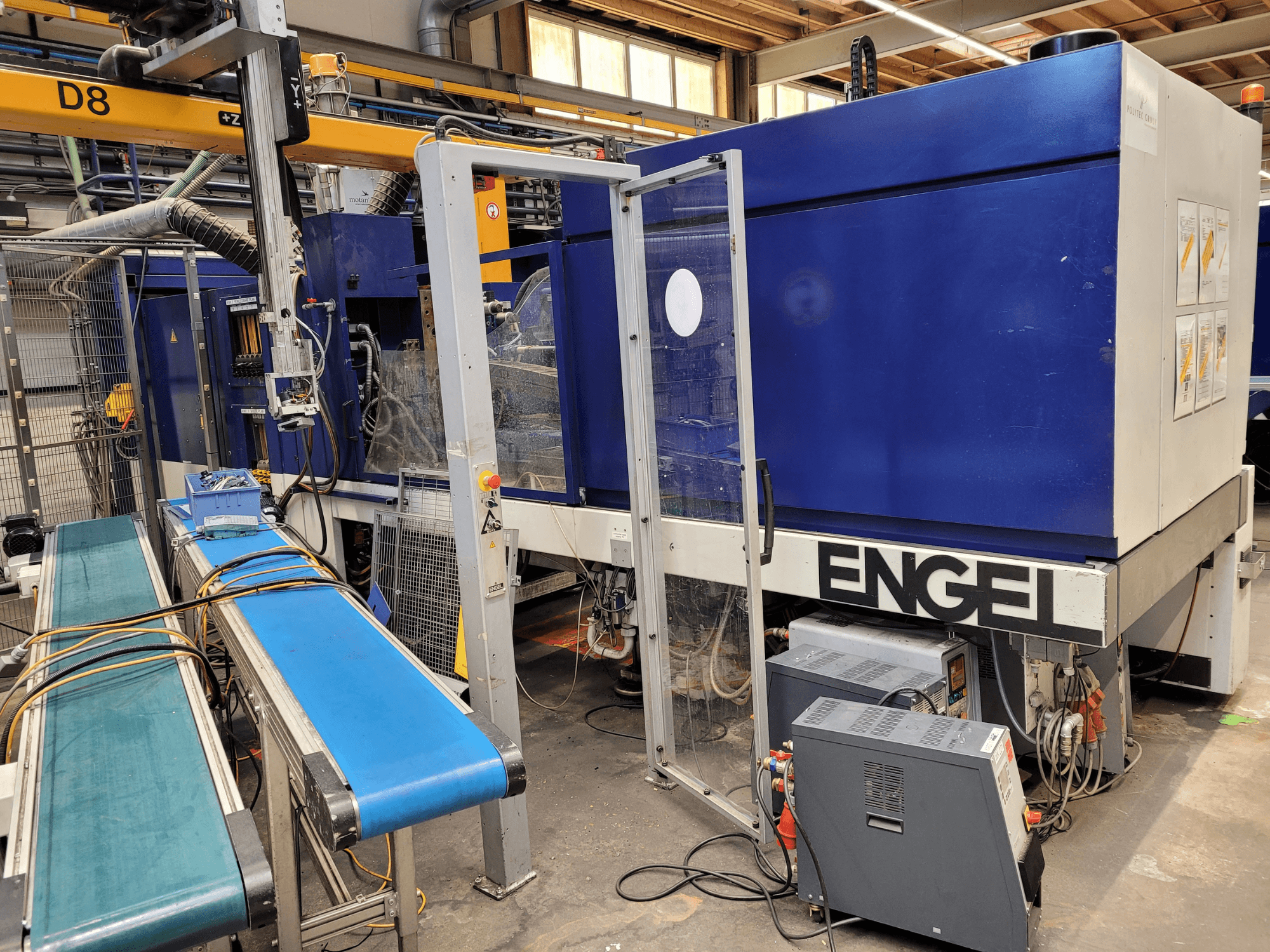 Blauwe ENGEL-machine met duidelijke veiligheidsdeur, zijaanzicht, met bedieningspaneel, transportband en zichtbare elektrische aansluitingen.