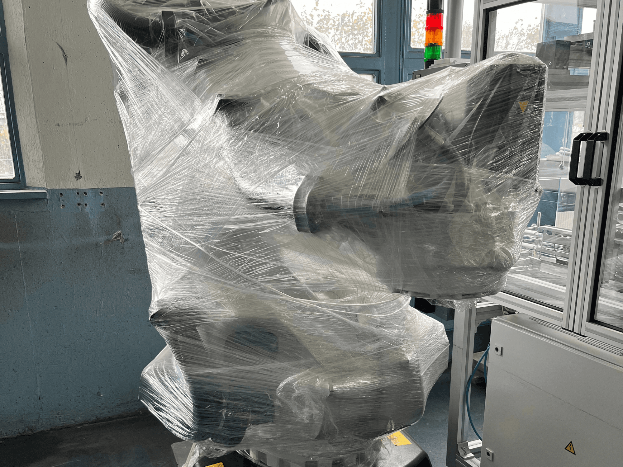 Industriële robotarm verpakt in plastic, vooraanzicht. Inclusief besturingseenheid en indicatielampje. Merk niet zichtbaar.