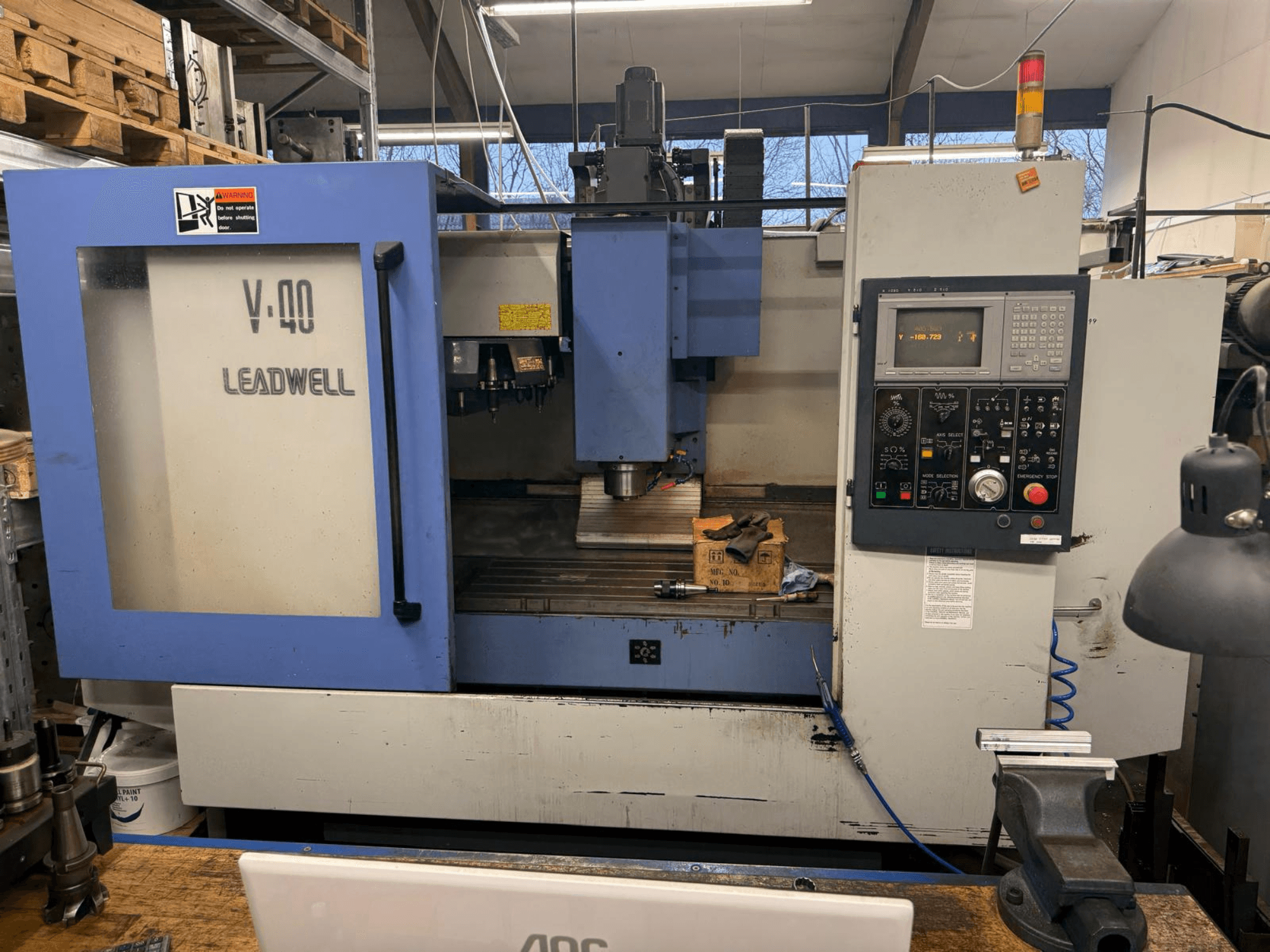 LEADWELL V-40 CNC freesmachine, vooraanzicht, met een bedieningspaneel, snijgereedschappen en een bankschroef op een werkbank.