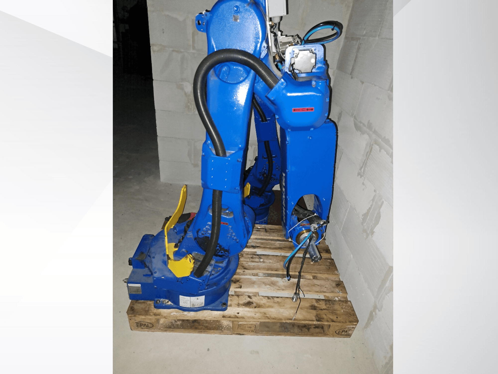Yaskawa Motoman GP25-robotarm in het blauw, zijaanzicht op een houten pallet, met kabels en mechanische scharnieren.