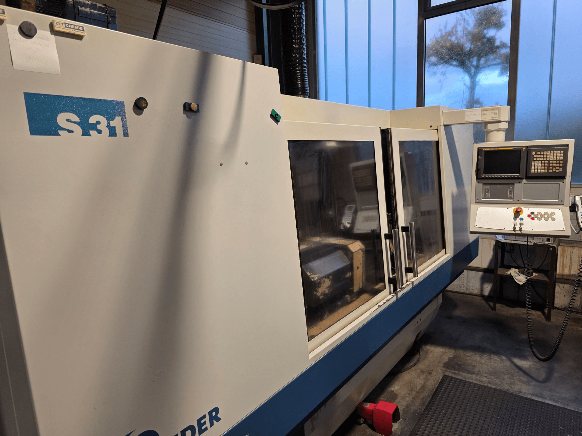 S31 CNC slijpmachine, vooraanzicht, voorzien van bedieningspaneel met scherm en knoppen, grote glazen deur, industriële omgeving.