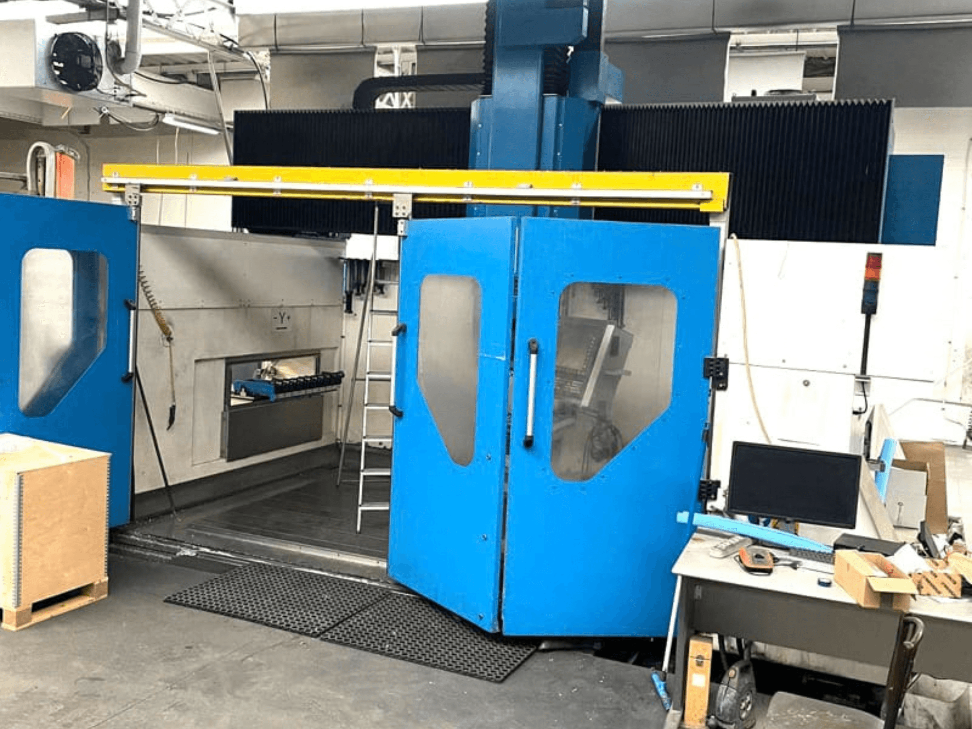 Vooraanzicht van het verticale bewerkingscentrum TECHMILL LABOR SHAPE 3220 met geopende blauwe deuren, waardoor het werkgebied binnenin zichtbaar is.