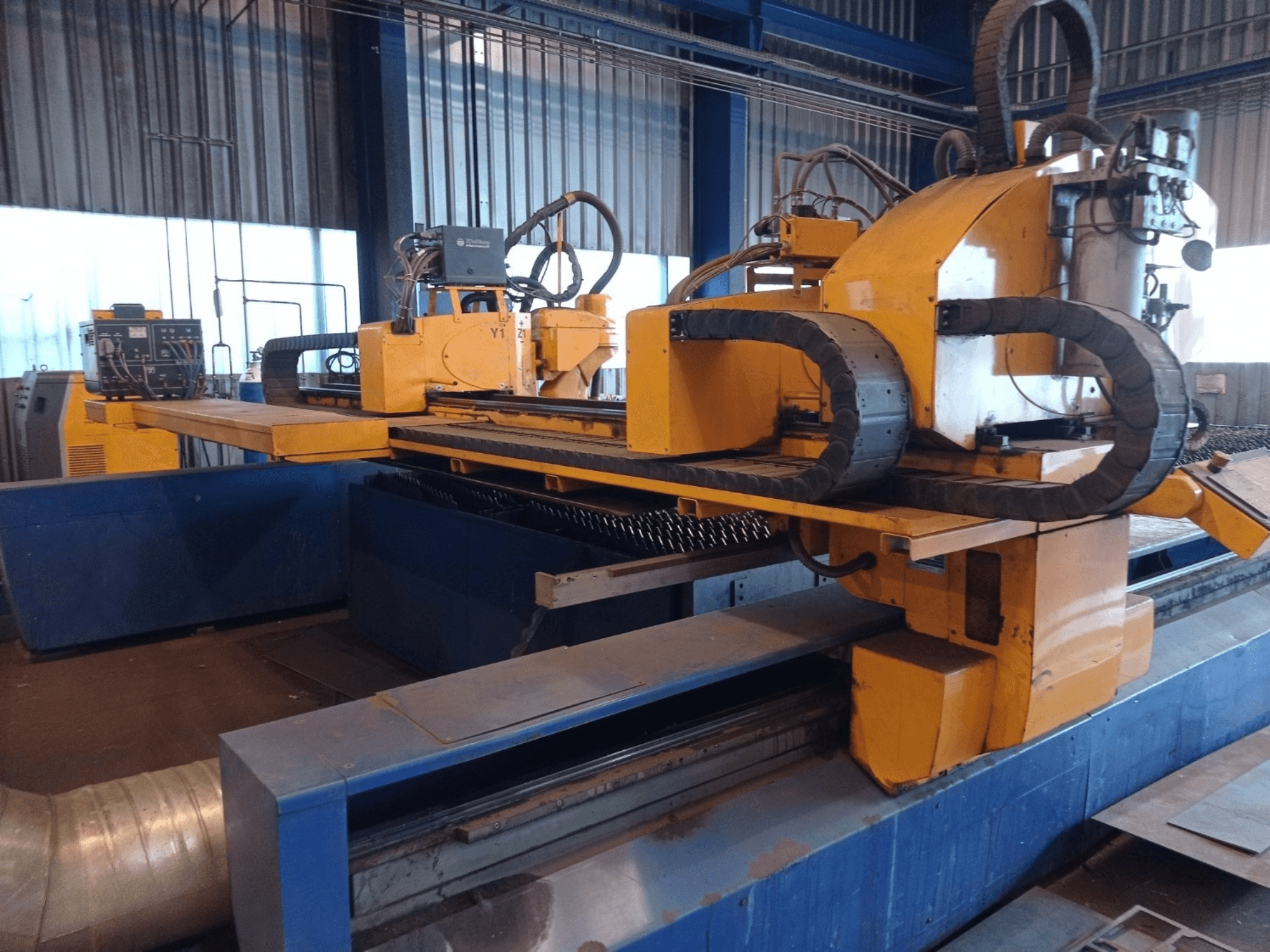 Gele CNC-plasmasnijmachine met twee horizontale armen, getoond vanaf de voorkant, met bedieningspaneel en snijbed.