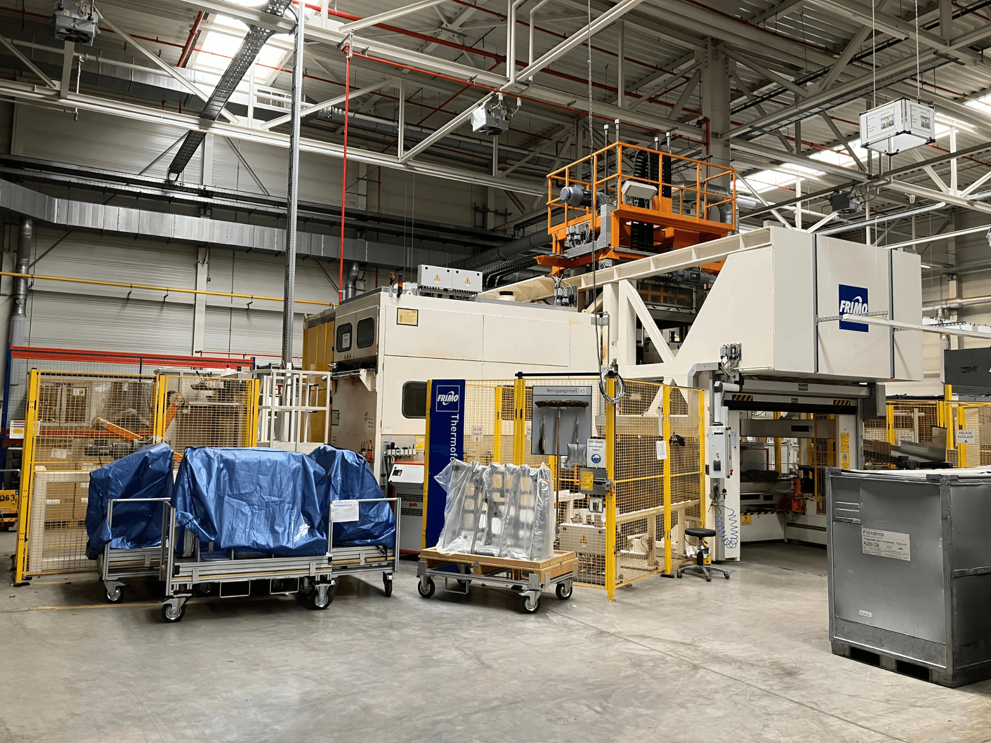 FRIMO FTL 80/200 Fullflex kunststofverwerkingsmachine in een fabriek, vooraanzicht met blauwe zeilen en veiligheidshekken zichtbaar.