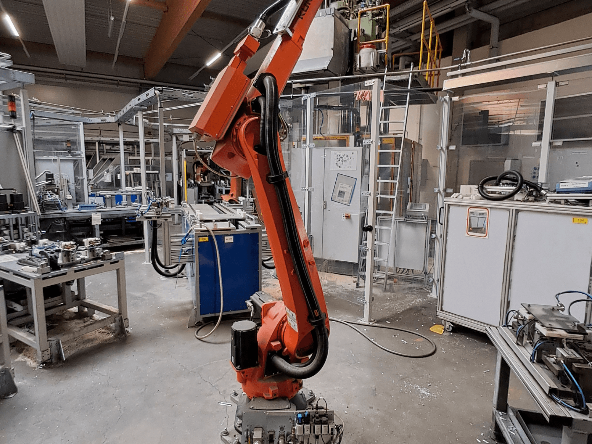 Een KUKA KR 26 R3100/SEL-robotarm in een industriële omgeving, afgebeeld in zijaanzicht met operationele apparatuur op de achtergrond.