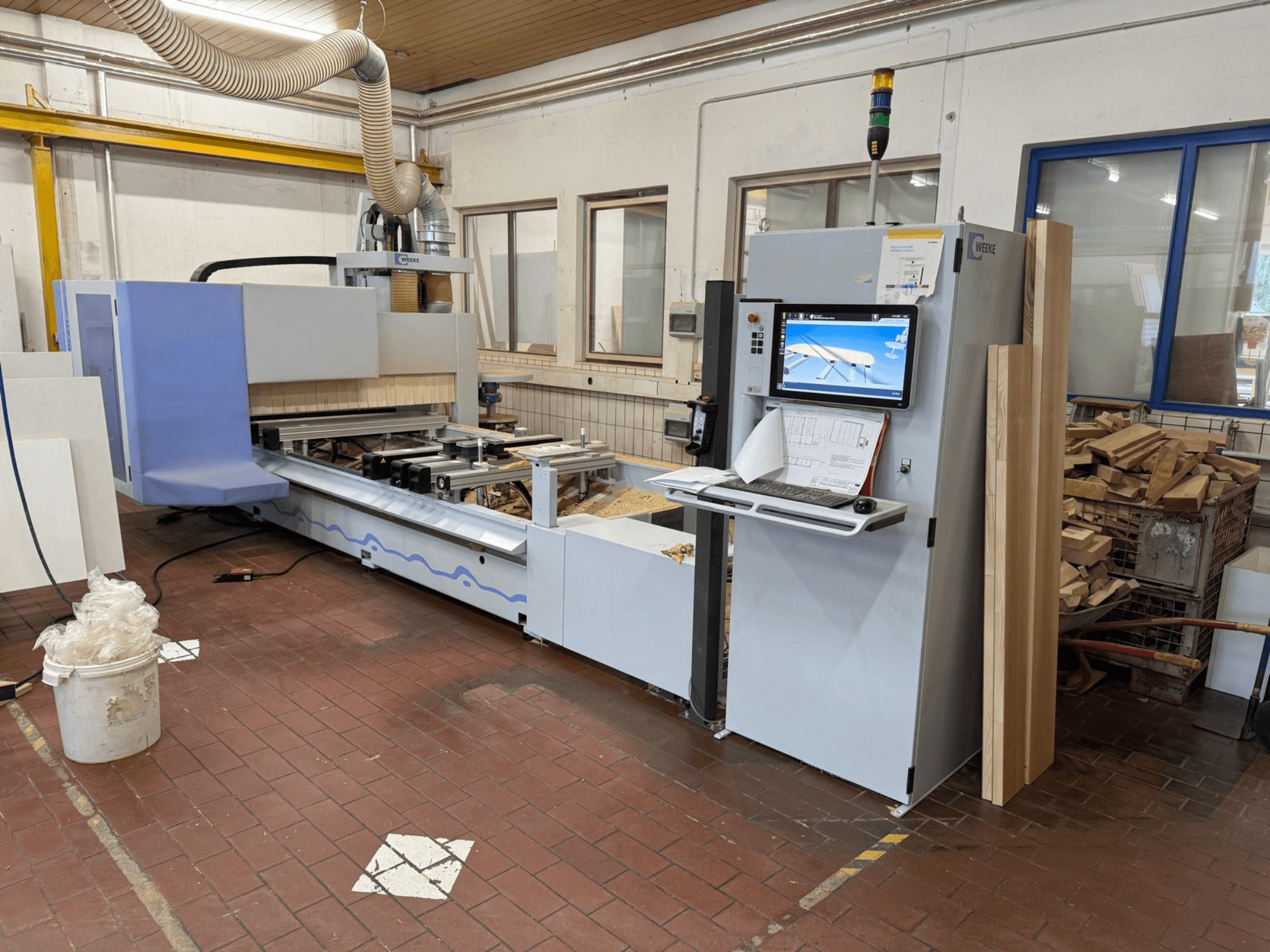 Weeke PROFI BMG211/32/12/K CNC-houtbewerkingscentrum, vooraanzicht, met bedieningspaneel en stukken hout, voorzien van een stofafzuigsysteem.