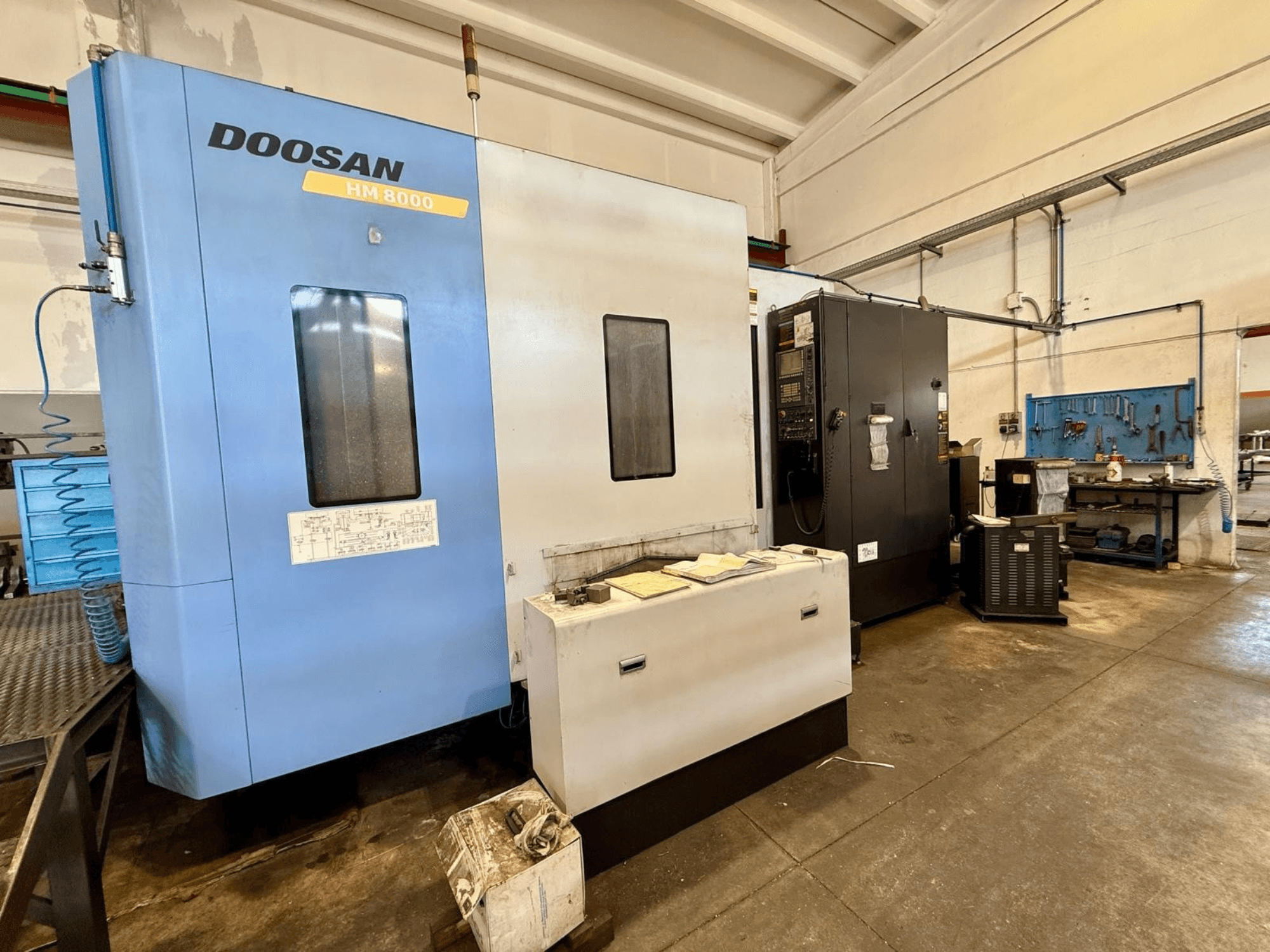 DOOSAN HM 8000 horizontaal bewerkingscentrum in blauw, vooraanzicht, met weergave van het bedieningspaneel en de werkplaatsapparatuur eromheen.