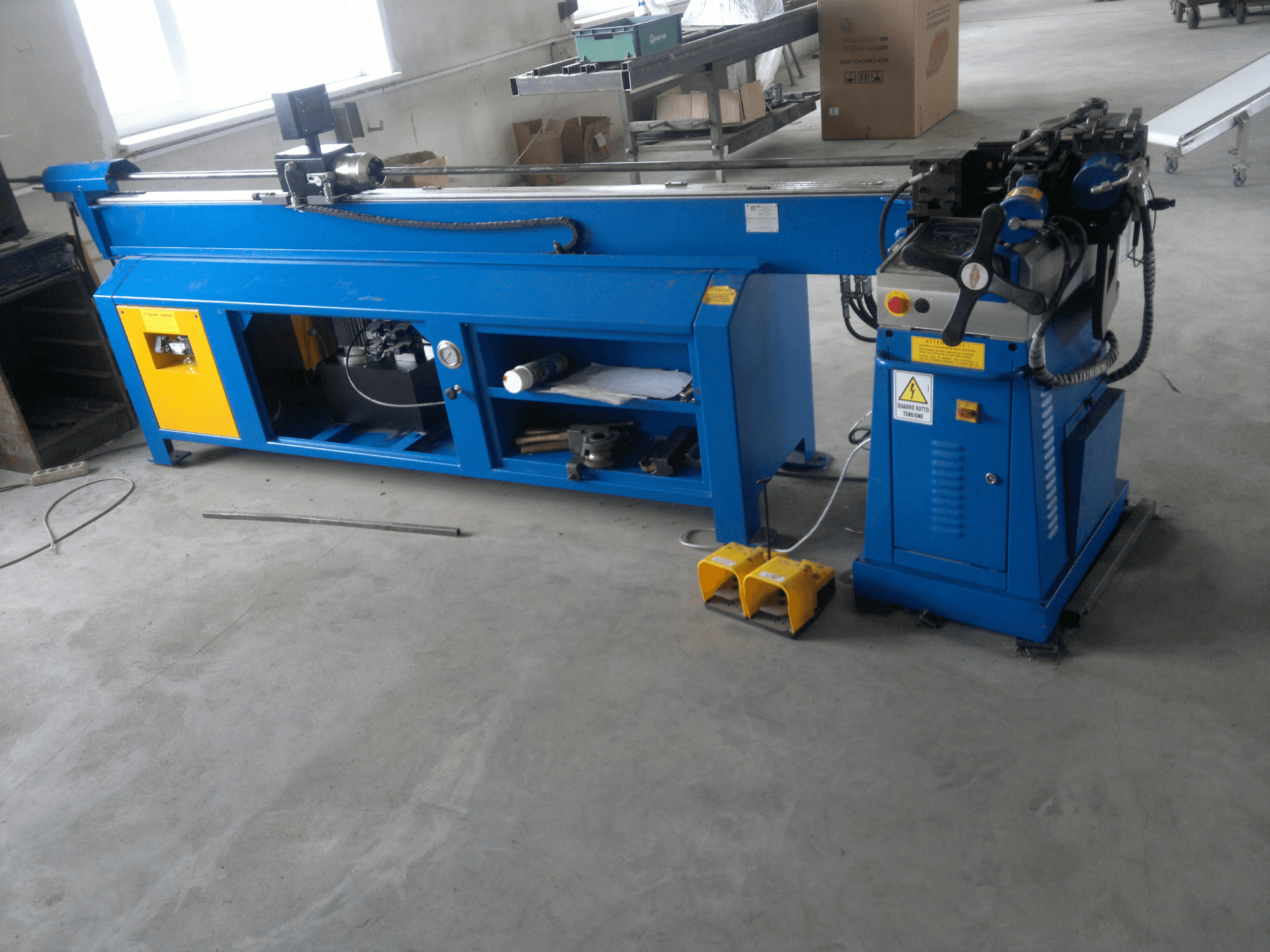 Blauwe houtbewerkingsmachine met gele accenten, zijaanzicht; voorzien van bedieningspaneel, voetpedalen en een draaiend blad.