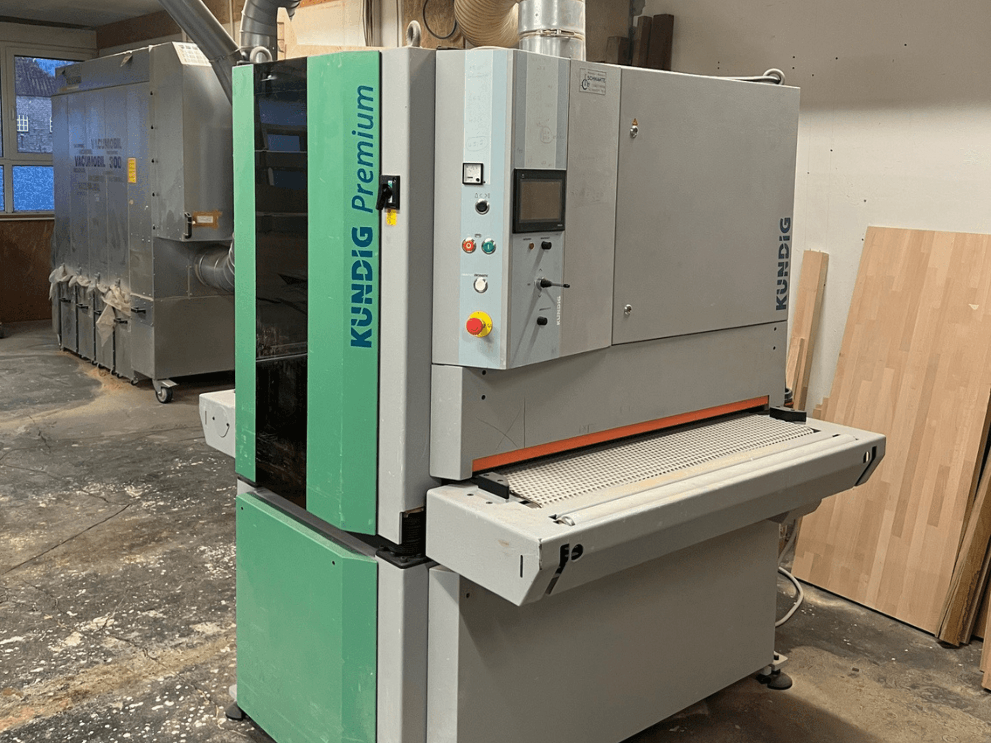 Kundig Premium-1 1100K bandschuurmachine in grijs en groen, afgebeeld in zijaanzicht met bedieningspaneel en schuurband zichtbaar.