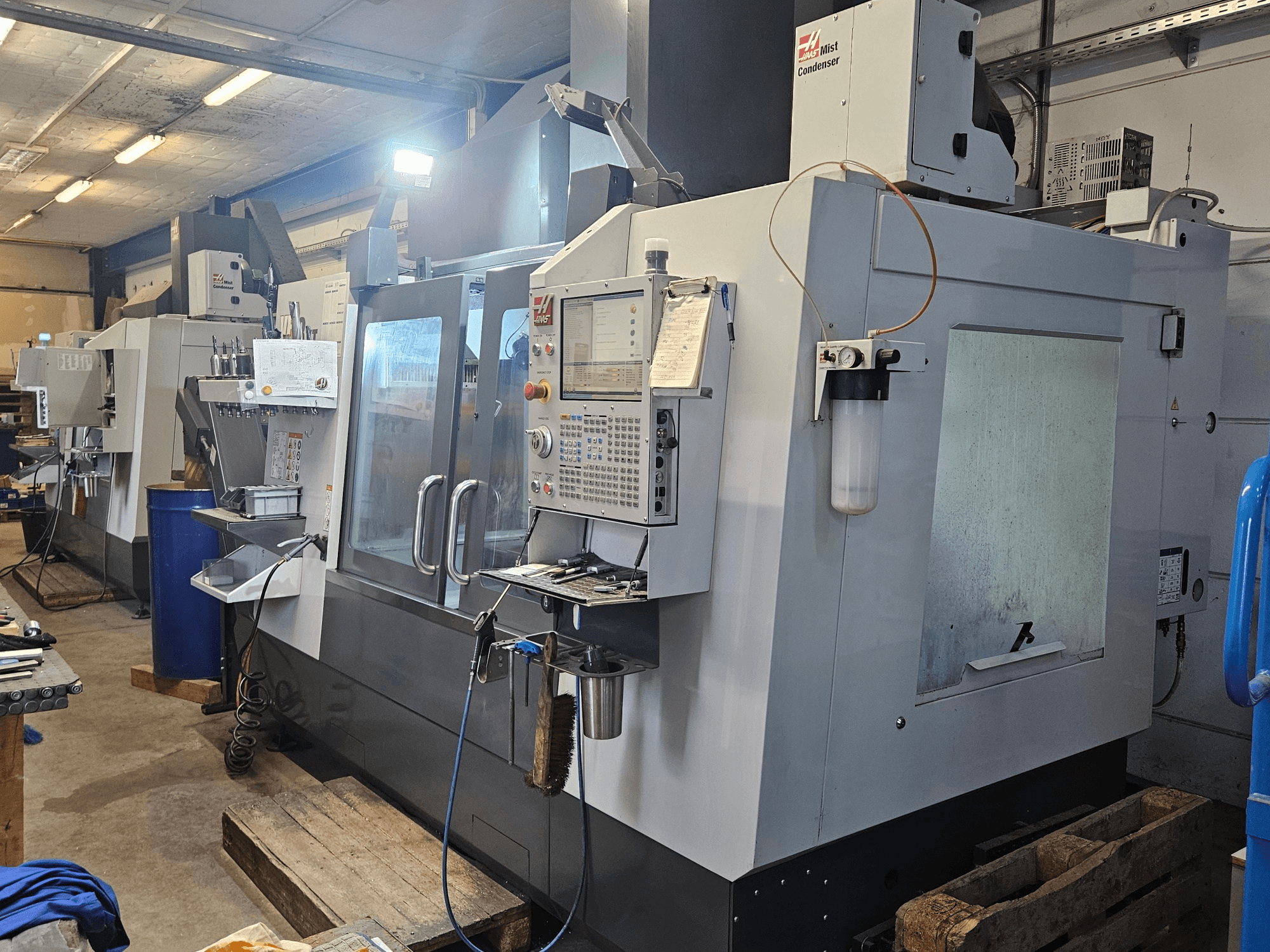 Haas VF-3YT/50 verticaal bewerkingscentrum in een werkplaats, vooraanzicht met bedieningspaneel, gereedschapshouders en nevelcondensor.