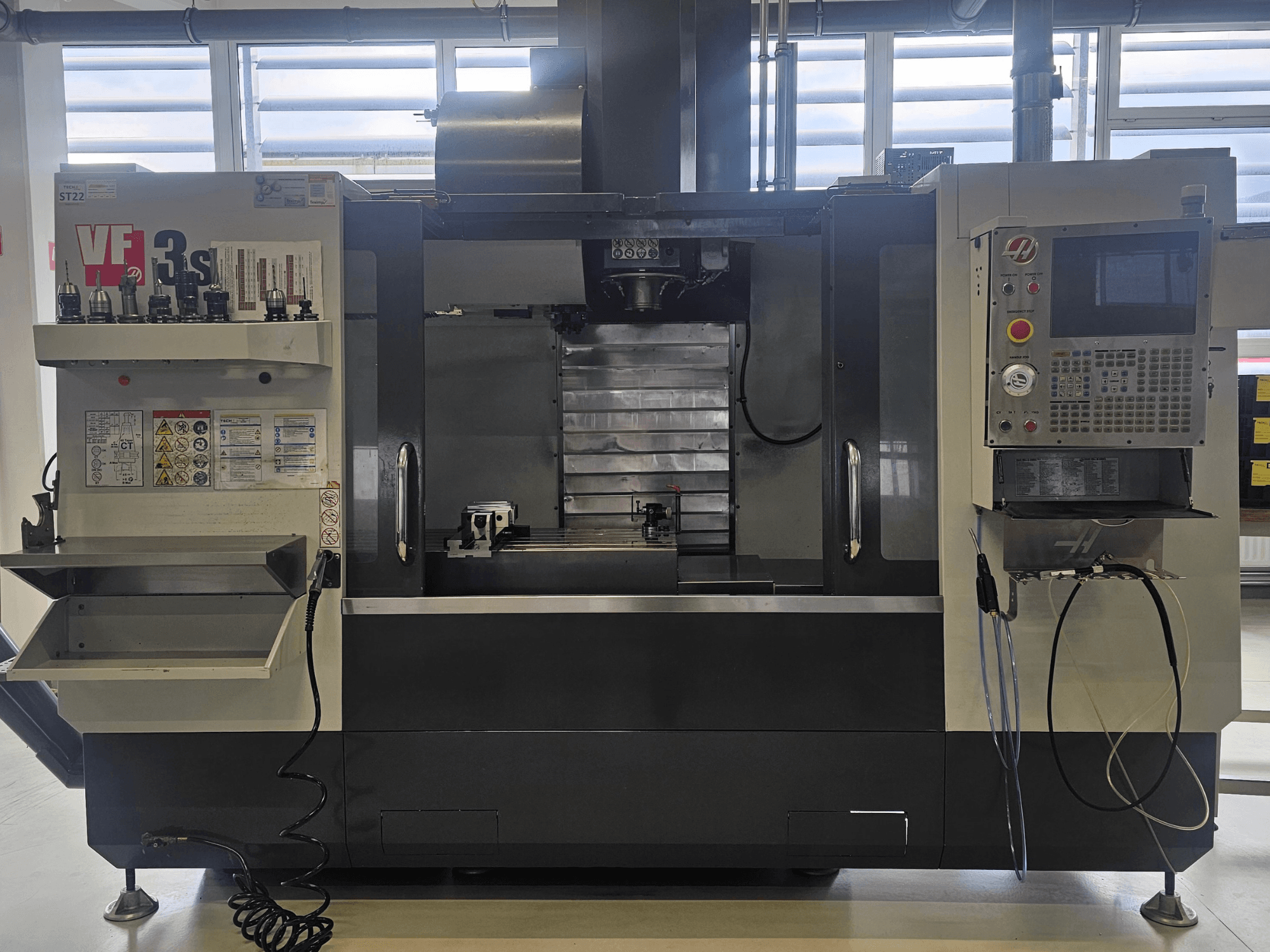 Haas VF3SS CNC-frees, vooraanzicht, met gereedschapshouders, bedieningspaneel en lege koelvloeistofbak, met veiligheidslabels zichtbaar.