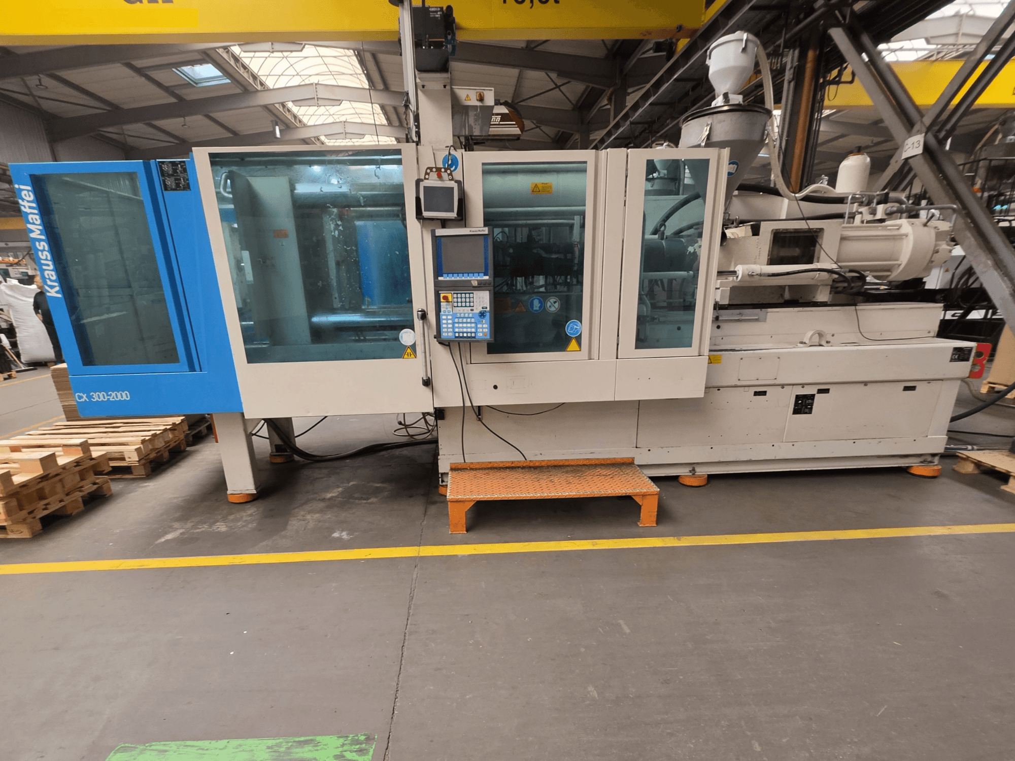 Krauss Maffei 300-2000 CX hydraulische spuitgietmachine, zijaanzicht met bedieningspaneel en grote ramen.