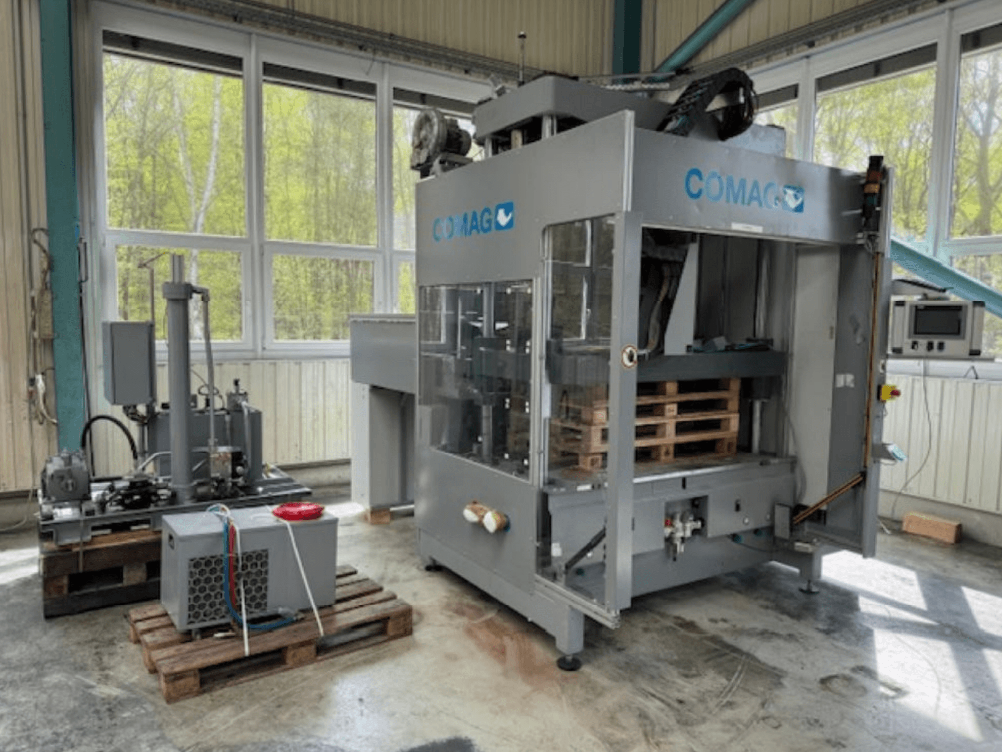 COMAG palletwikkelmachine in industriële omgeving, vooraanzicht; kenmerken pallets en hydraulische componenten zichtbaar.