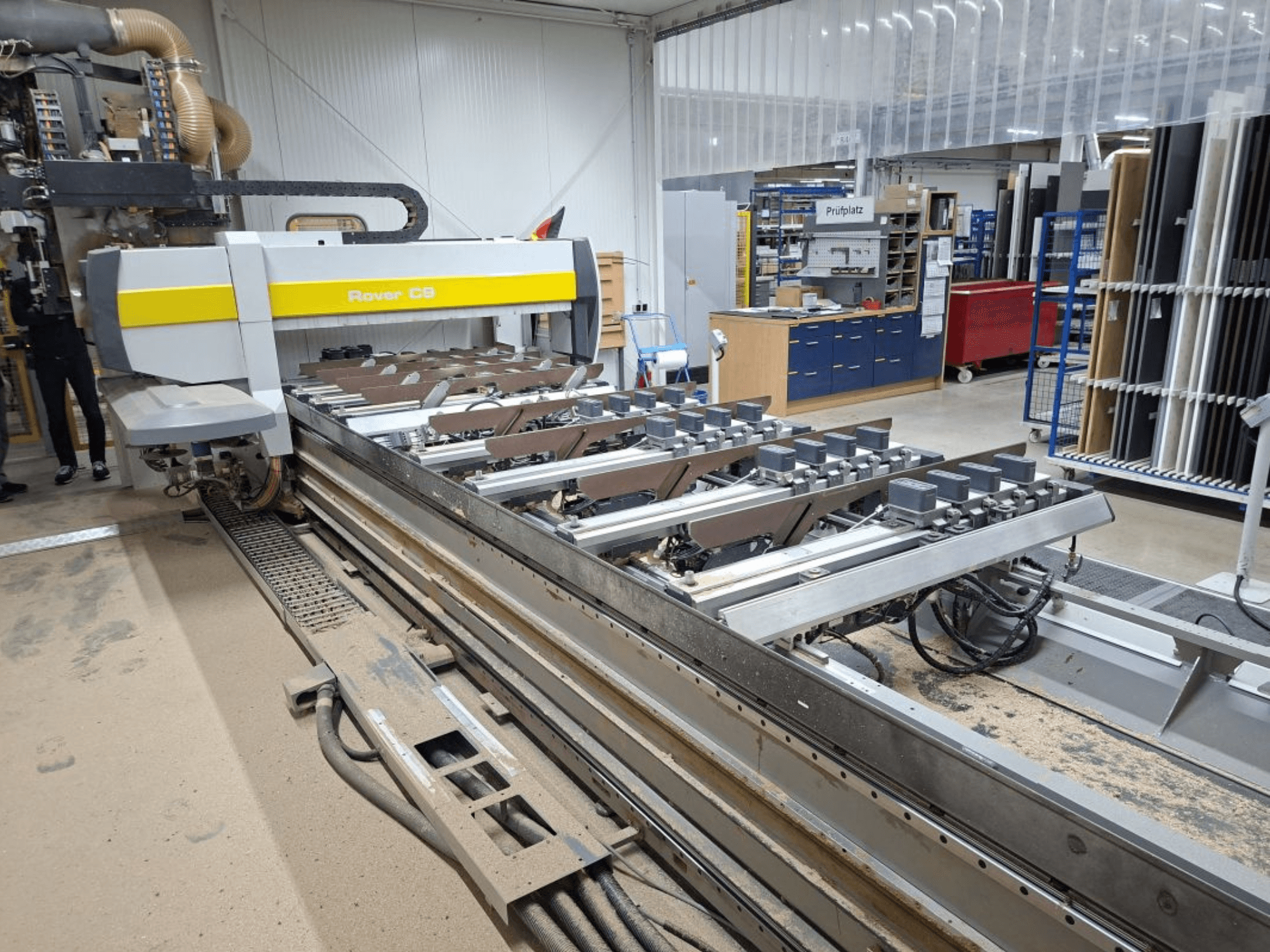 Rover C9 CNC machine in een werkplaats; vooraanzicht toont snijgereedschap en transportsysteem, met stofophoping op de vloer.