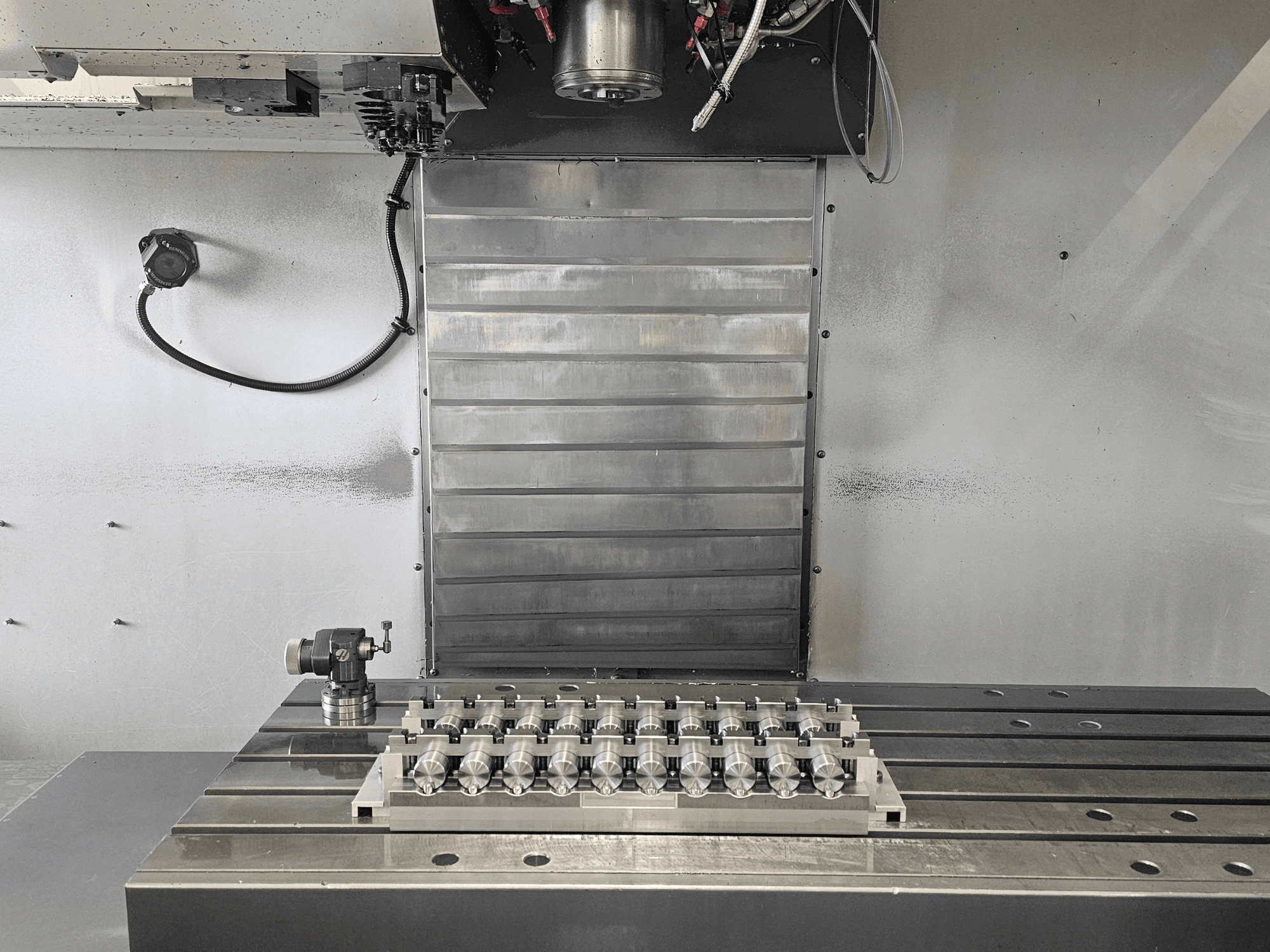 Vooraanzicht van de werkruimte van een CNC freesmachine met een precisiebewerkt onderdeel op een metalen tafel en bedieningsmechanismen.
