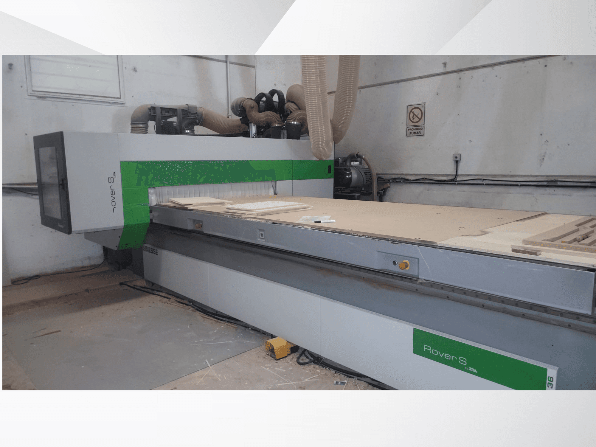 Vooraanzicht van de Biesse Rover S CNC machine, met een groot werkoppervlak met houten panelen en stofafzuigslangen.