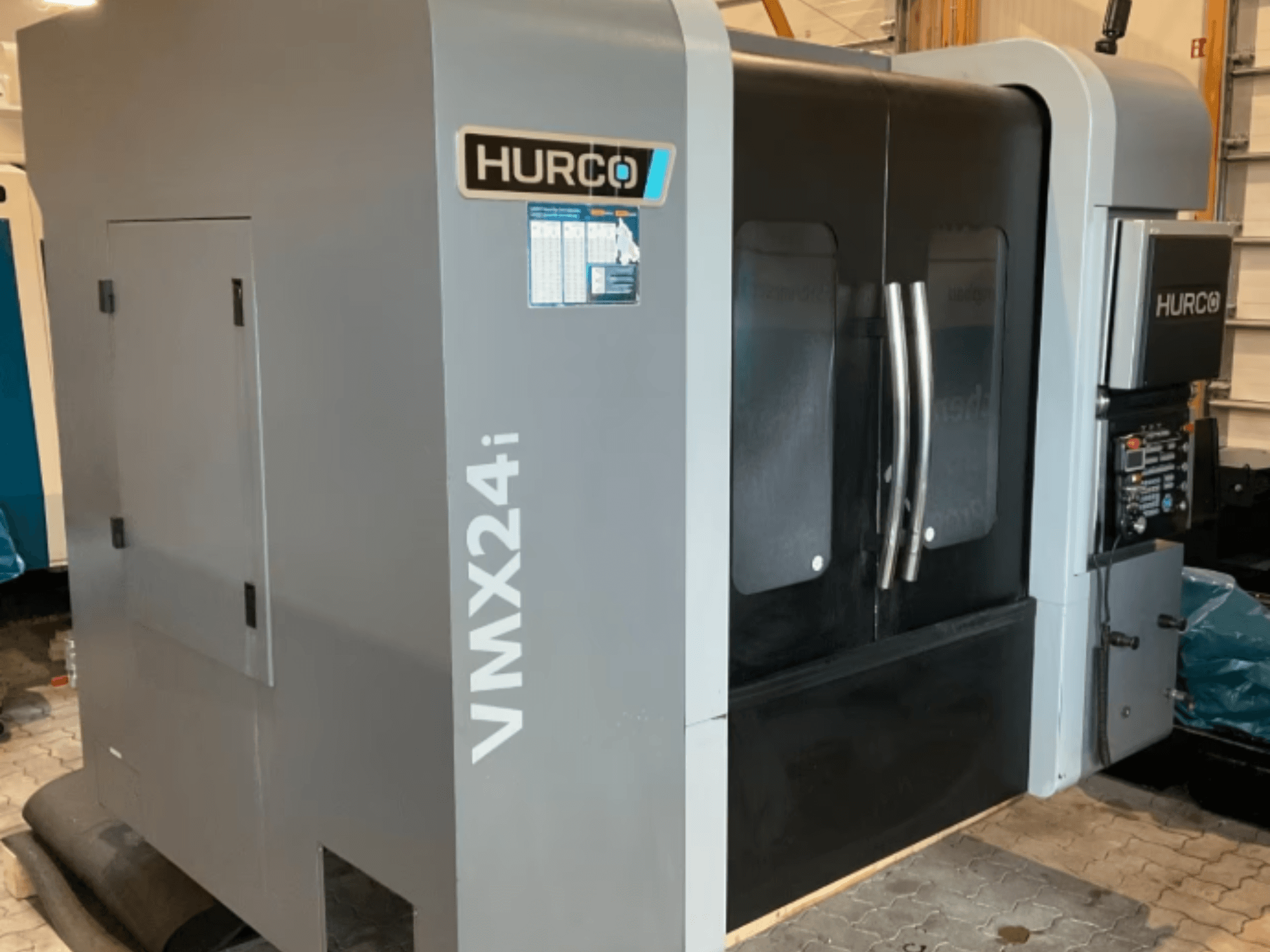 Hurco VMX 24i verticaal bewerkingscentrum, vooraanzicht met een metaalgrijze behuizing, zwarte paneeldeuren en bedieningspaneel.