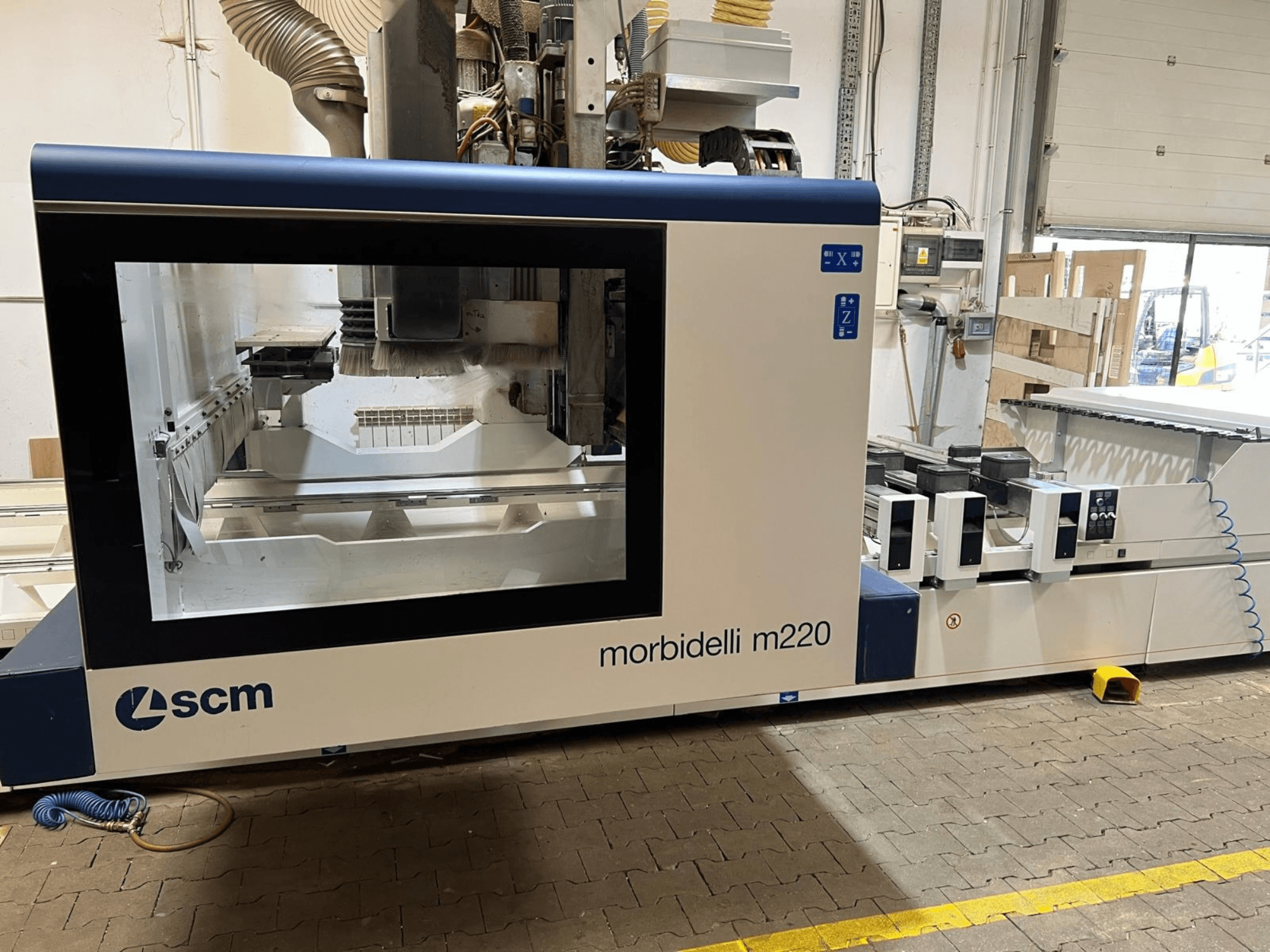 Vooraanzicht van het SCM Morbidelli M220 CNC-bewerkingscentrum, met een groot venster, bedieningspaneel en werkgebied.