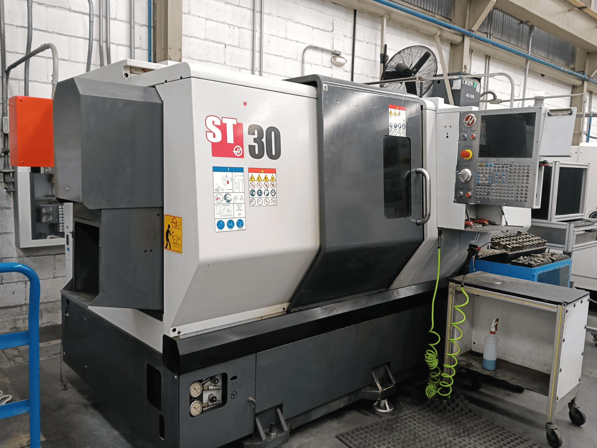 Alternatieve tekst: Vooraanzicht van de HAAS ST-30 horizontale draaimachine met bedieningspaneel, veiligheidsstickers en gereedschap op een karretje ernaast.