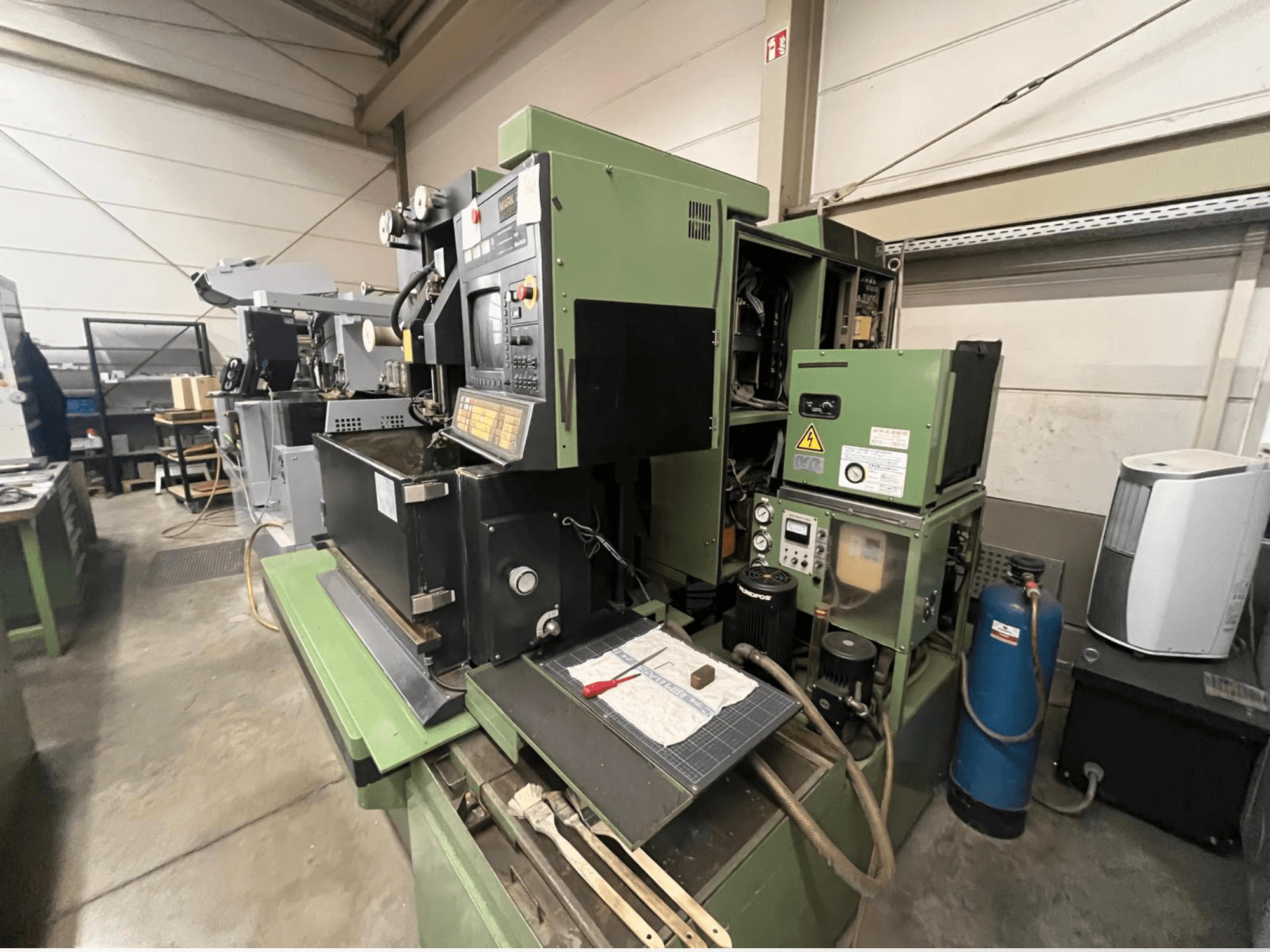 Groene industriële machine met bedieningspaneel, zijaanzicht; inclusief hydraulische onderdelen en werkruimte met gereedschap.