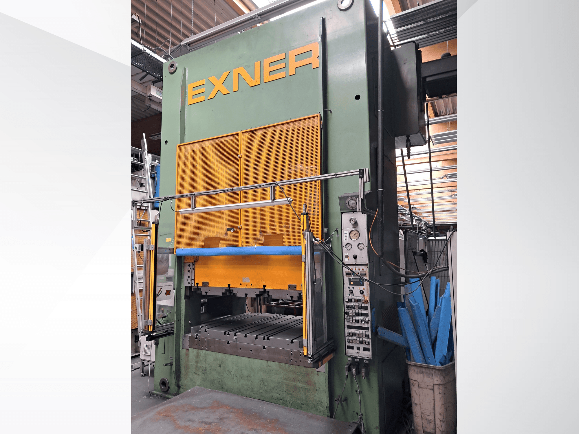 Hydraulische pers EXNER EX SBR 150, vooraanzicht; met bedieningselementen, blauwe veiligheidsbeugel en gaasafscherming, geplaatst in een werkplaatsomgeving.