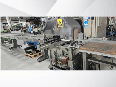 Industriële snijmachine in zijaanzicht, met een lange transportband, bedieningspaneel en veiligheidswaarschuwingen.