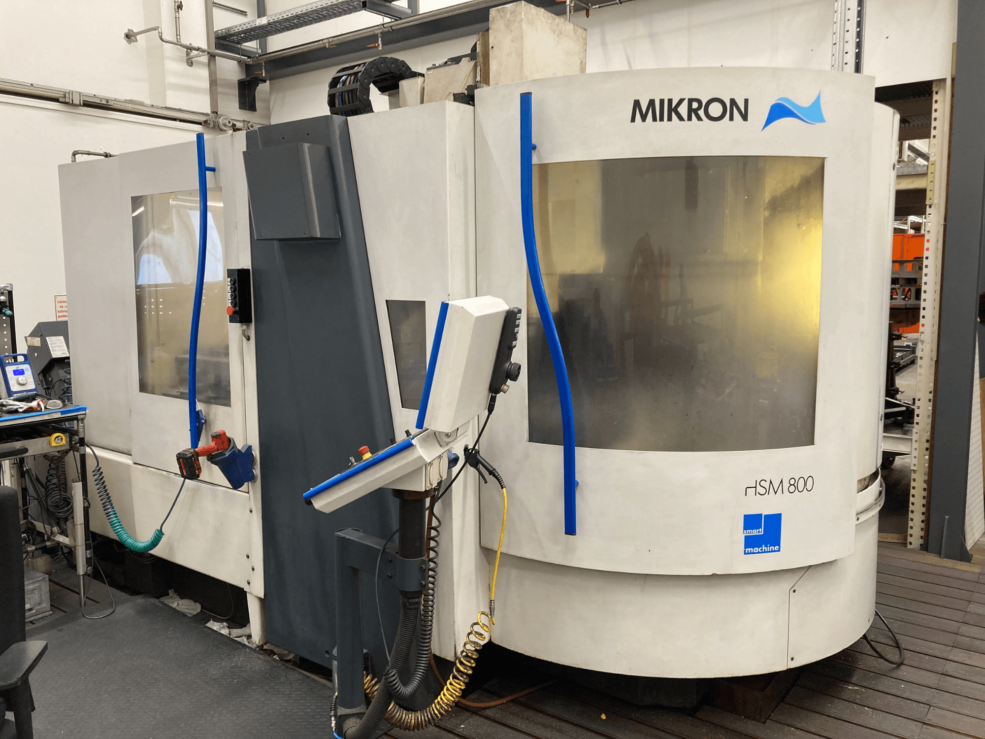 Mikron HSM 800, zijaanzicht van een CNC-bewerkingscentrum met bedieningspaneel en gereedschaphouder, zichtbare slangen en kabels.
